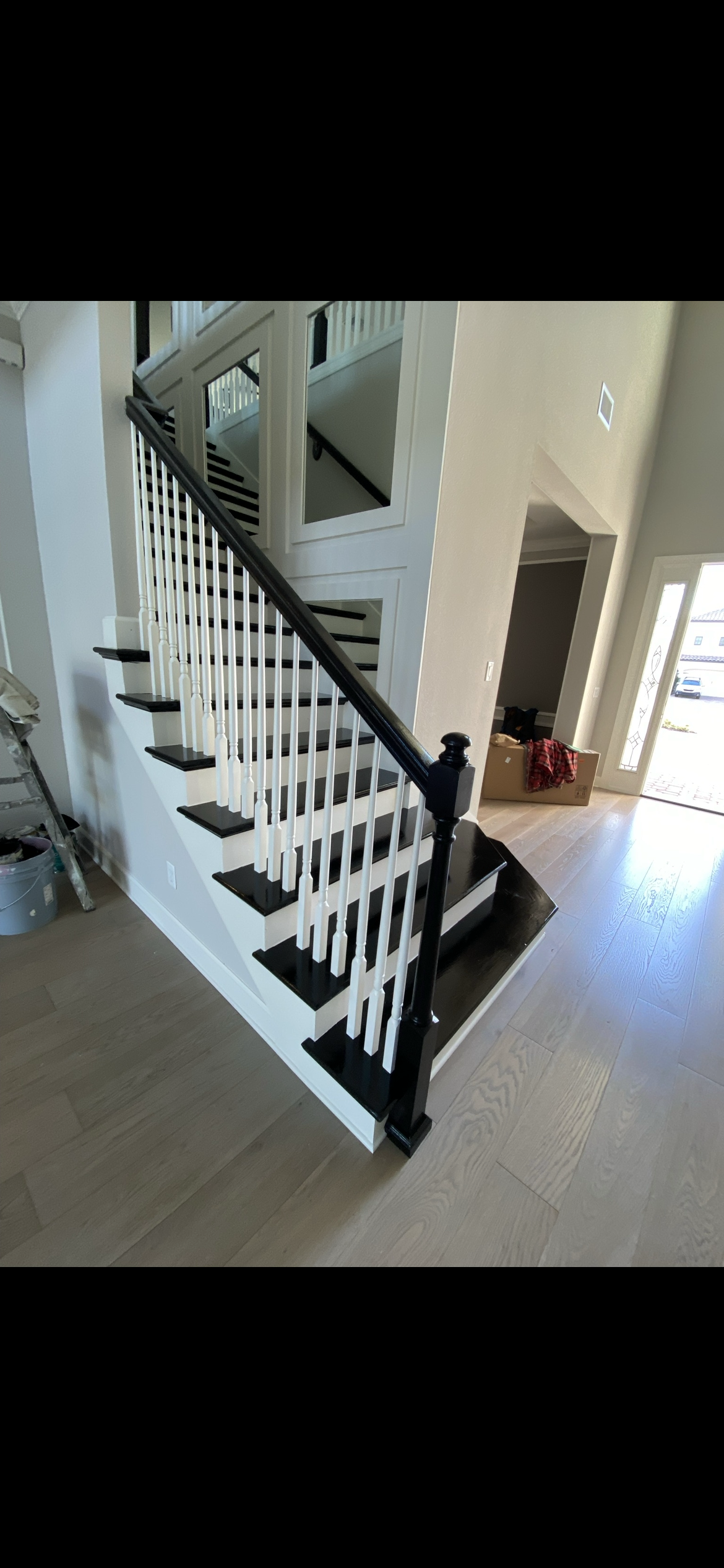 Staircase with black banister and steps, white spindles, and light wood flooring in a bright interior.