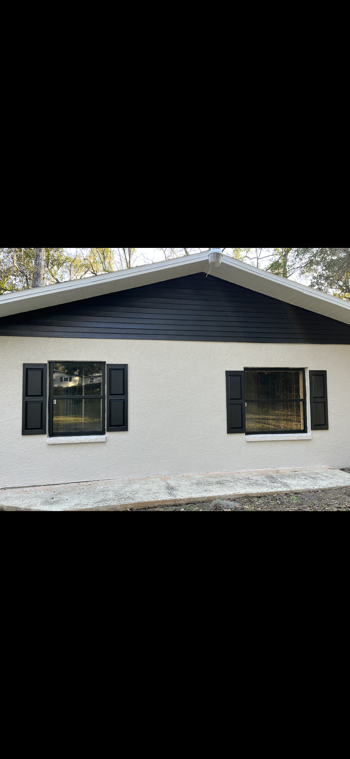White stucco building with black roof and shutters; two windows.