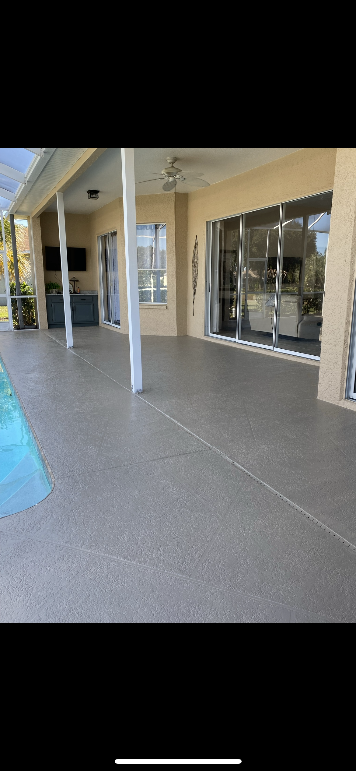 A covered patio with a pool in the foreground. The patio has gray flooring, pillars, and glass doors.
