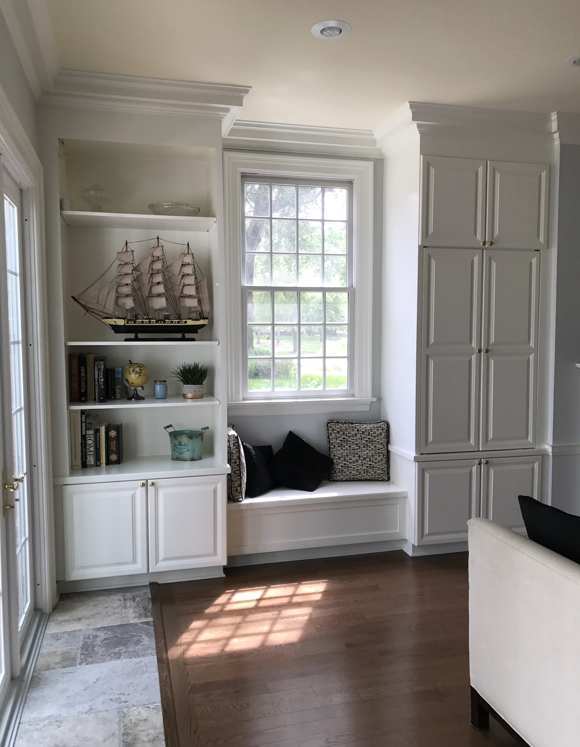 Built-in white shelves and cabinets flank a window with a cushioned window seat.