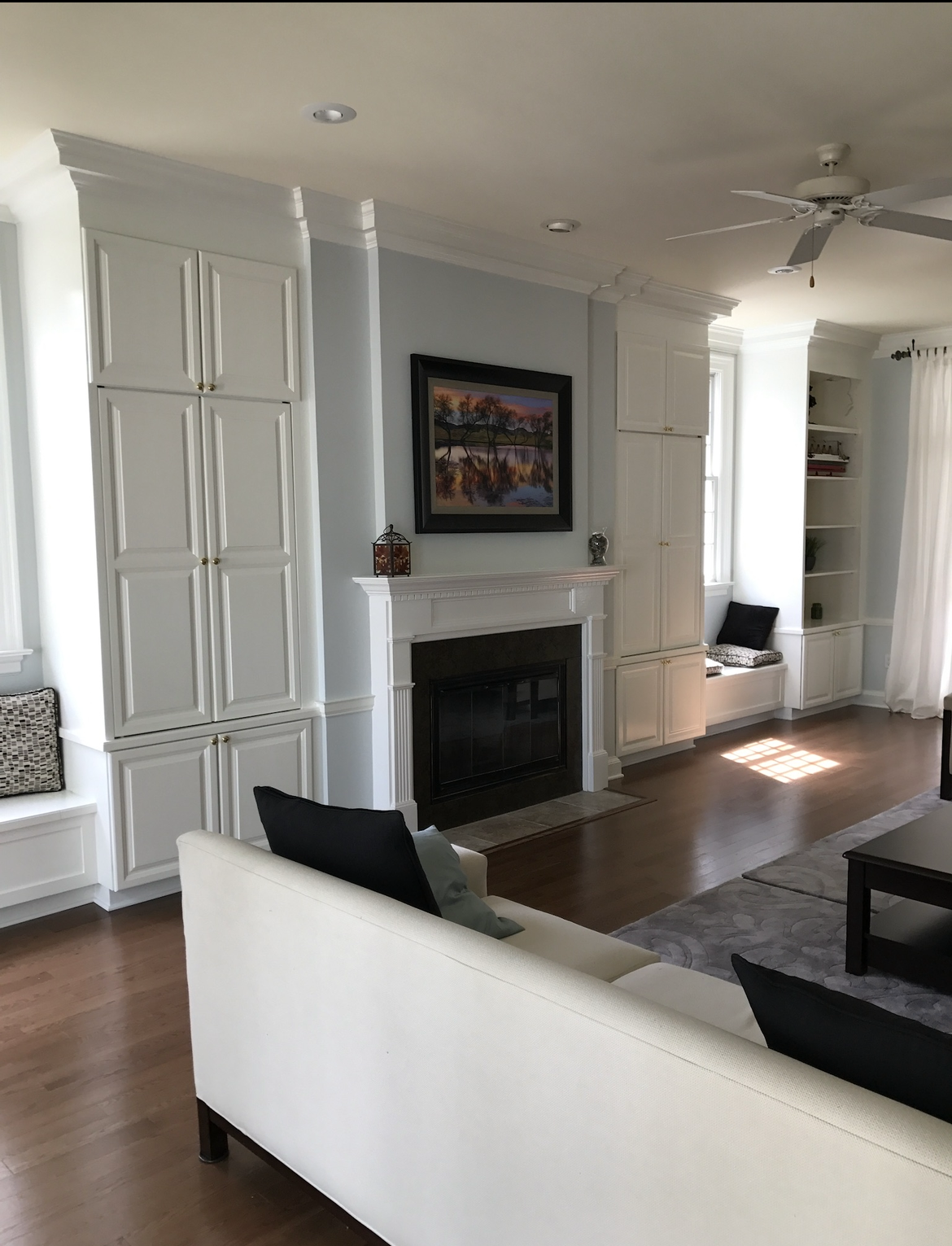 Living room with white built-in cabinets and fireplace. Wooden floor and white couch.
