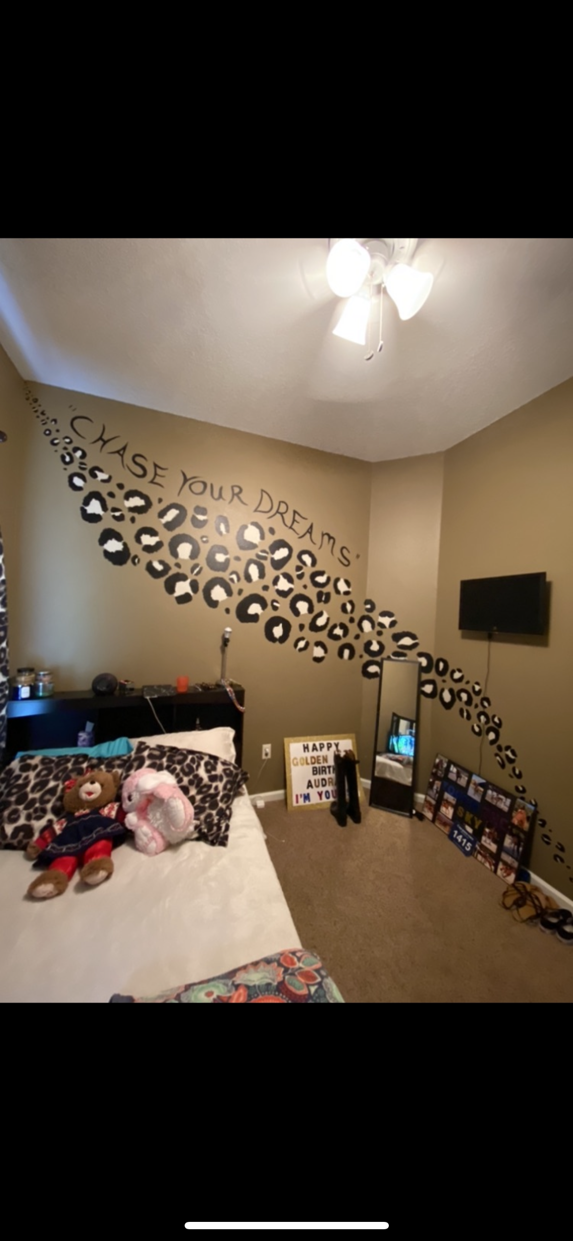 Bedroom with wall decor, a bed, a TV, and a sign that says, “Chase Your Dreams”.
