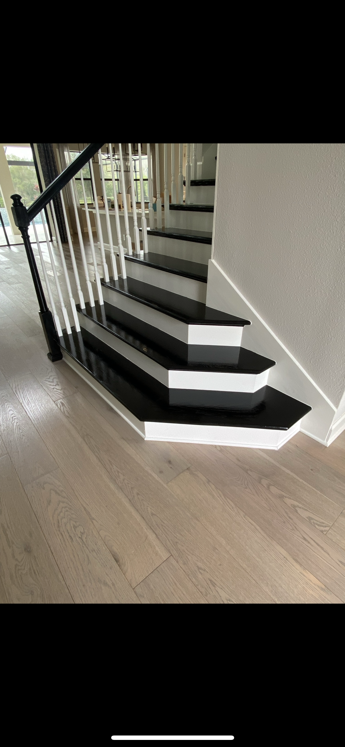 Staircase with black treads, white risers, and a white balustrade with a black handrail. Light wood floors.