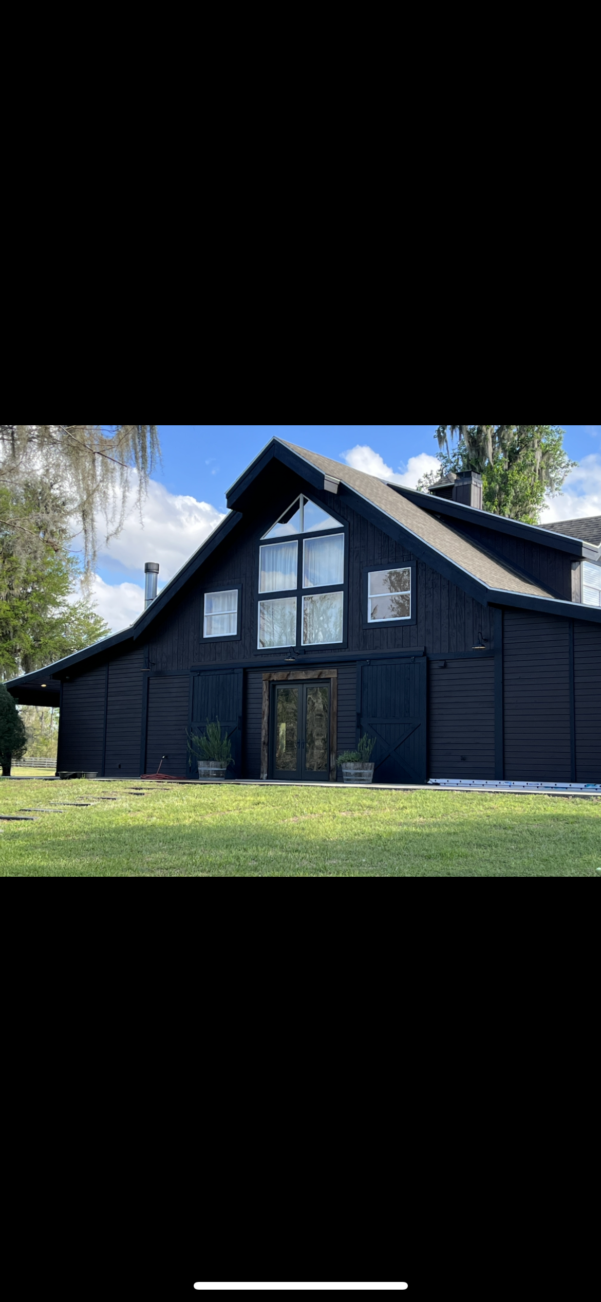 Black barn-style house with large windows and a green lawn under a blue sky.