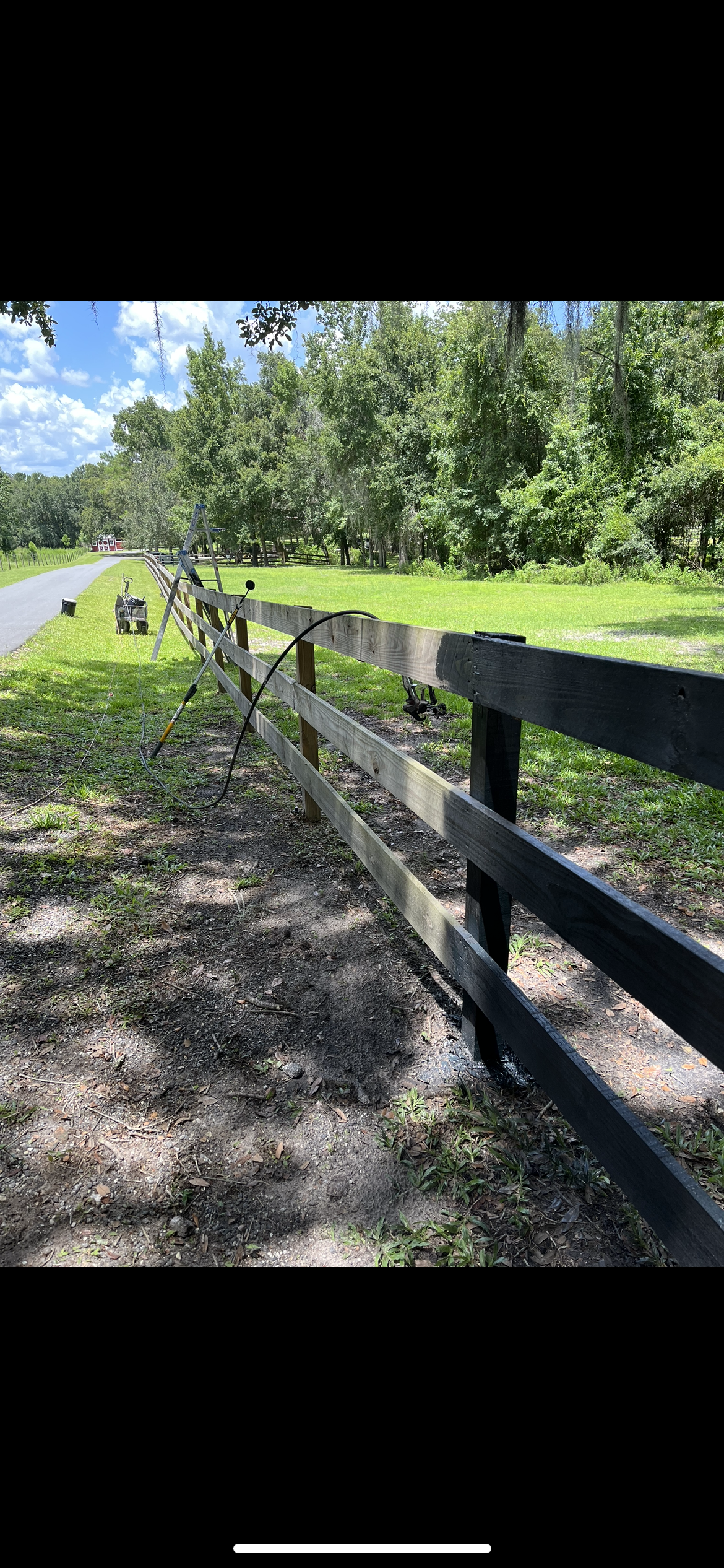 Wooden fence alongside a path, leading into a wooded area on a sunny day.
