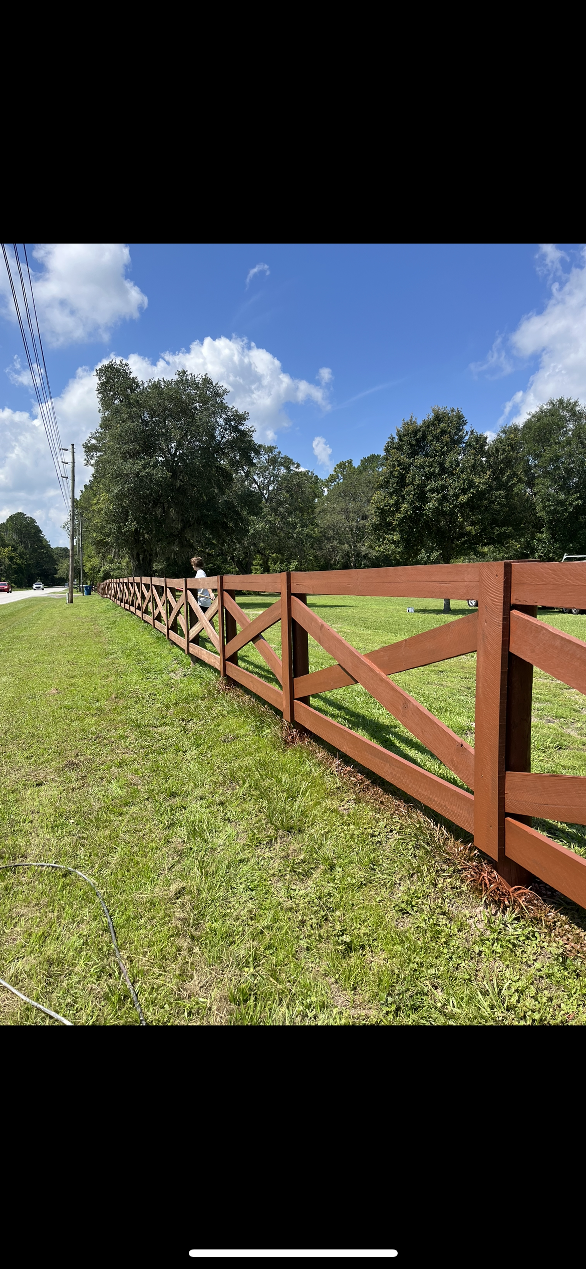 Brown wooden fence in a grassy field, under a blue sky with clouds.