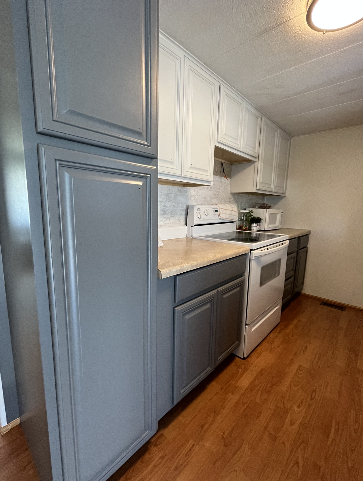 Kitchen with gray and white cabinets, white appliances, and wood flooring.