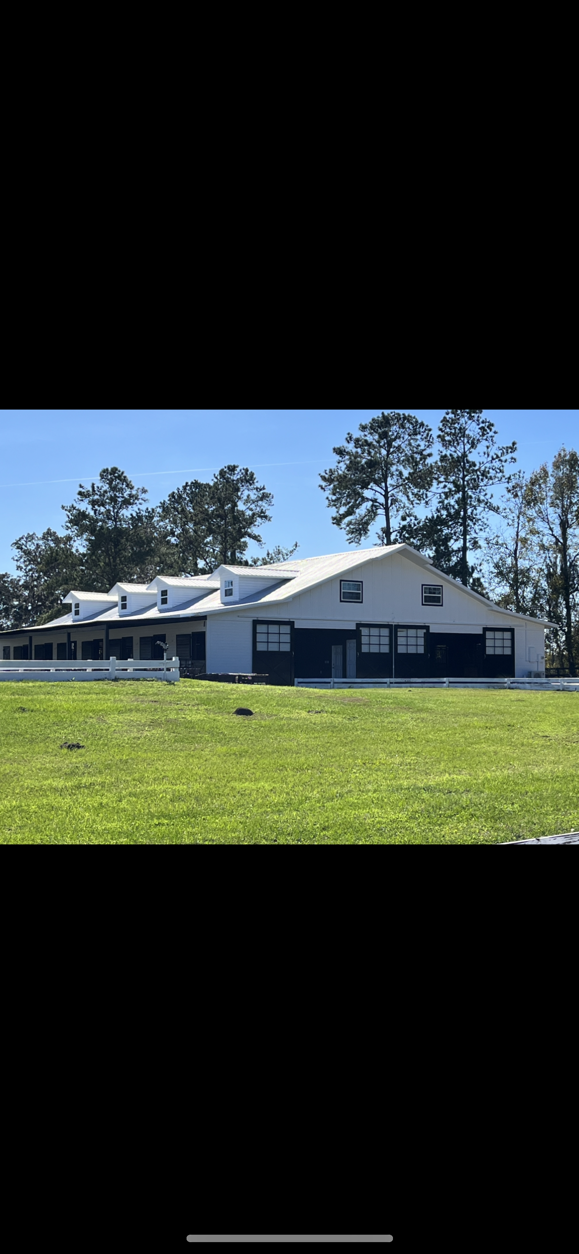White farmhouse with a white fence, situated on a green lawn with a blue sky background.