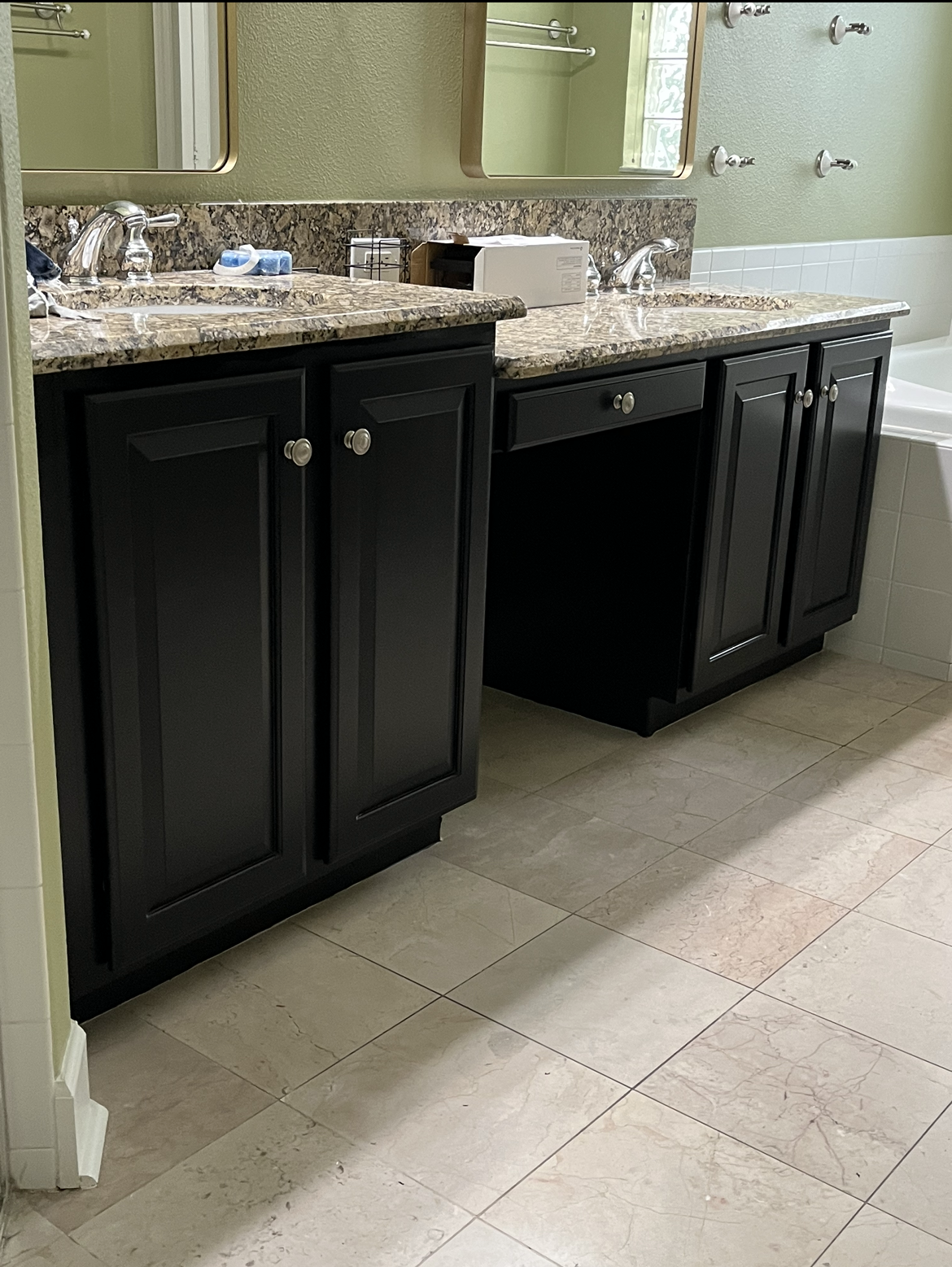 Black bathroom cabinets with granite countertop and cream-colored tile flooring.