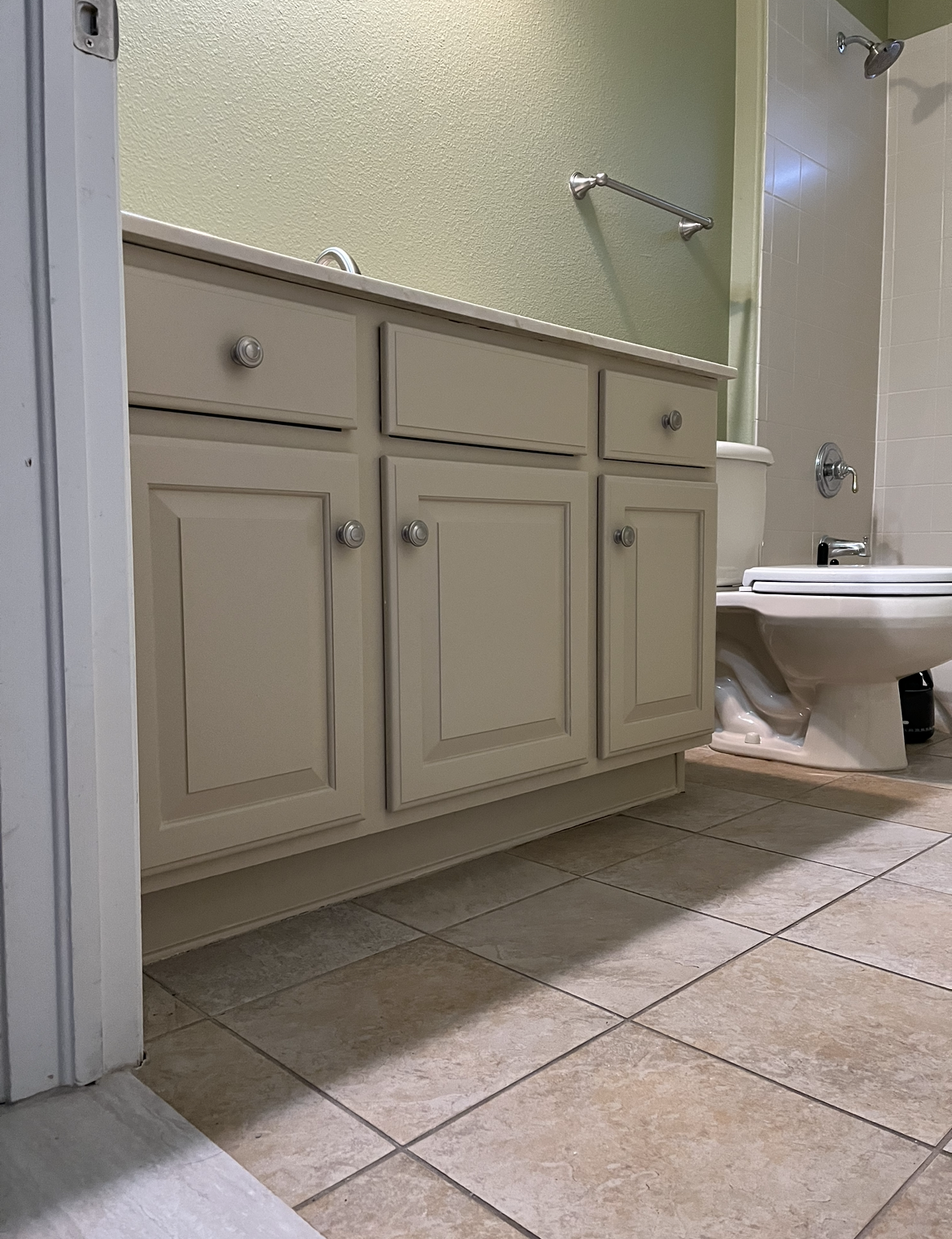Bathroom vanity with cabinets, toilet, and tile floor. Beige cabinets, pale green wall, and white toilet.