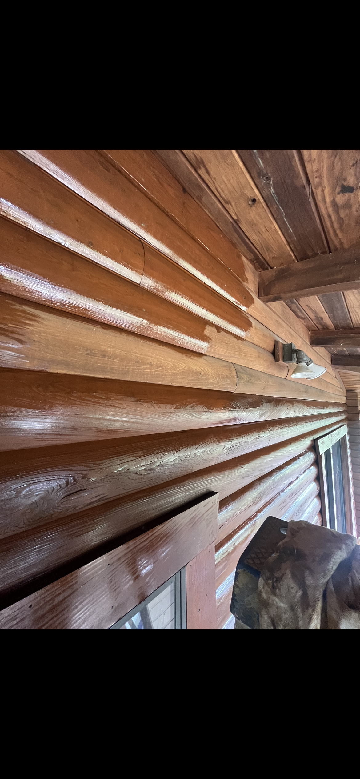Wooden exterior of a cabin, showing the siding and eaves, with a glimpse of an interior space.