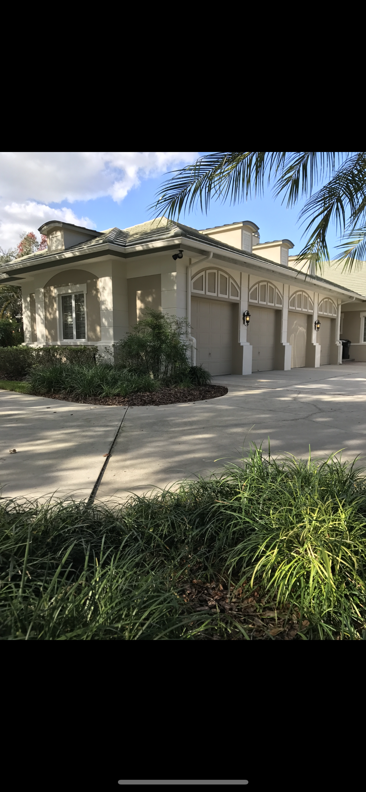 Light-colored building with multiple garage doors and arches; surrounded by greenery and a driveway.