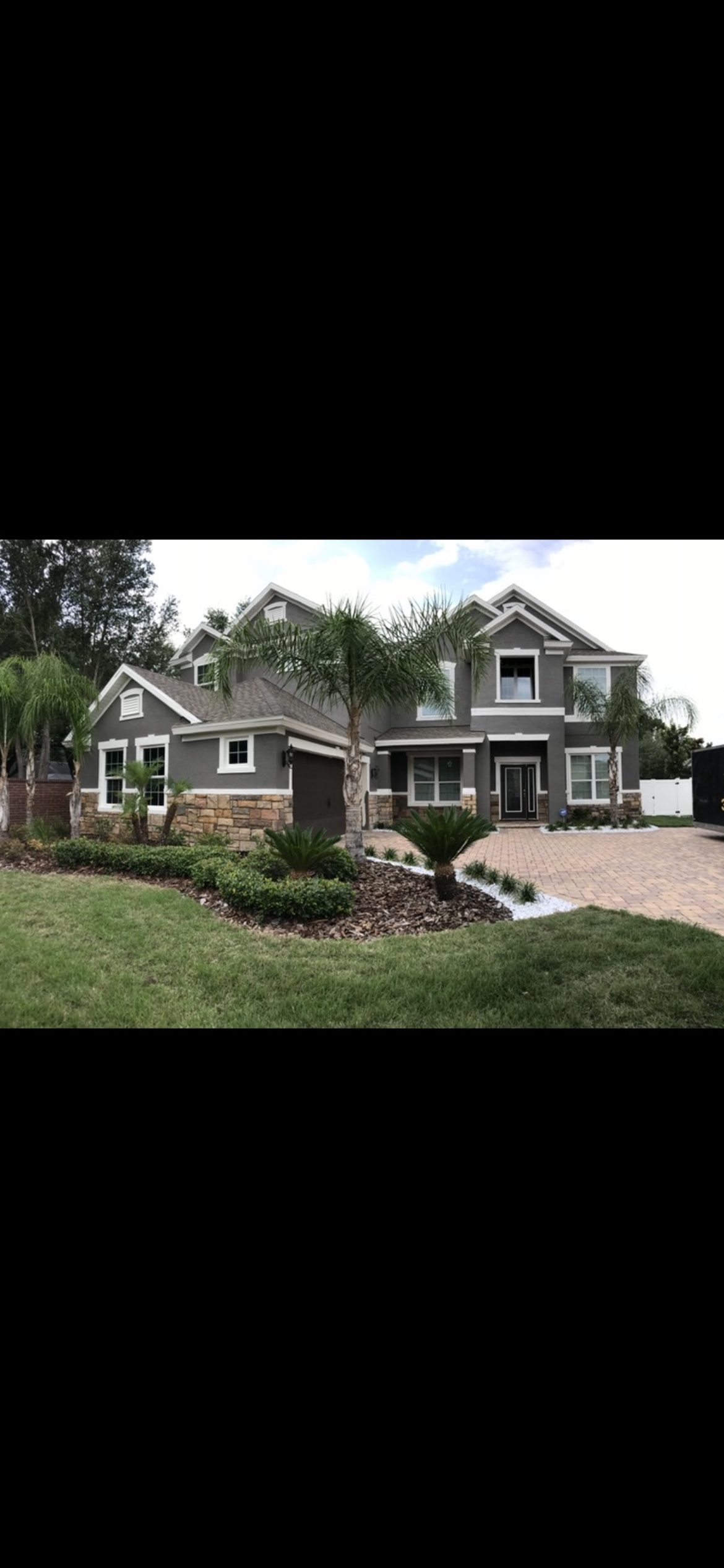 A two-story gray house with stone accents, a lawn, and trees.