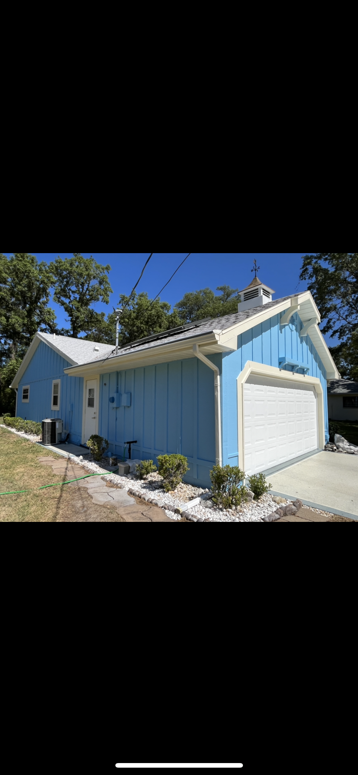 Blue house with white trim and garage door; green trees and blue sky background.