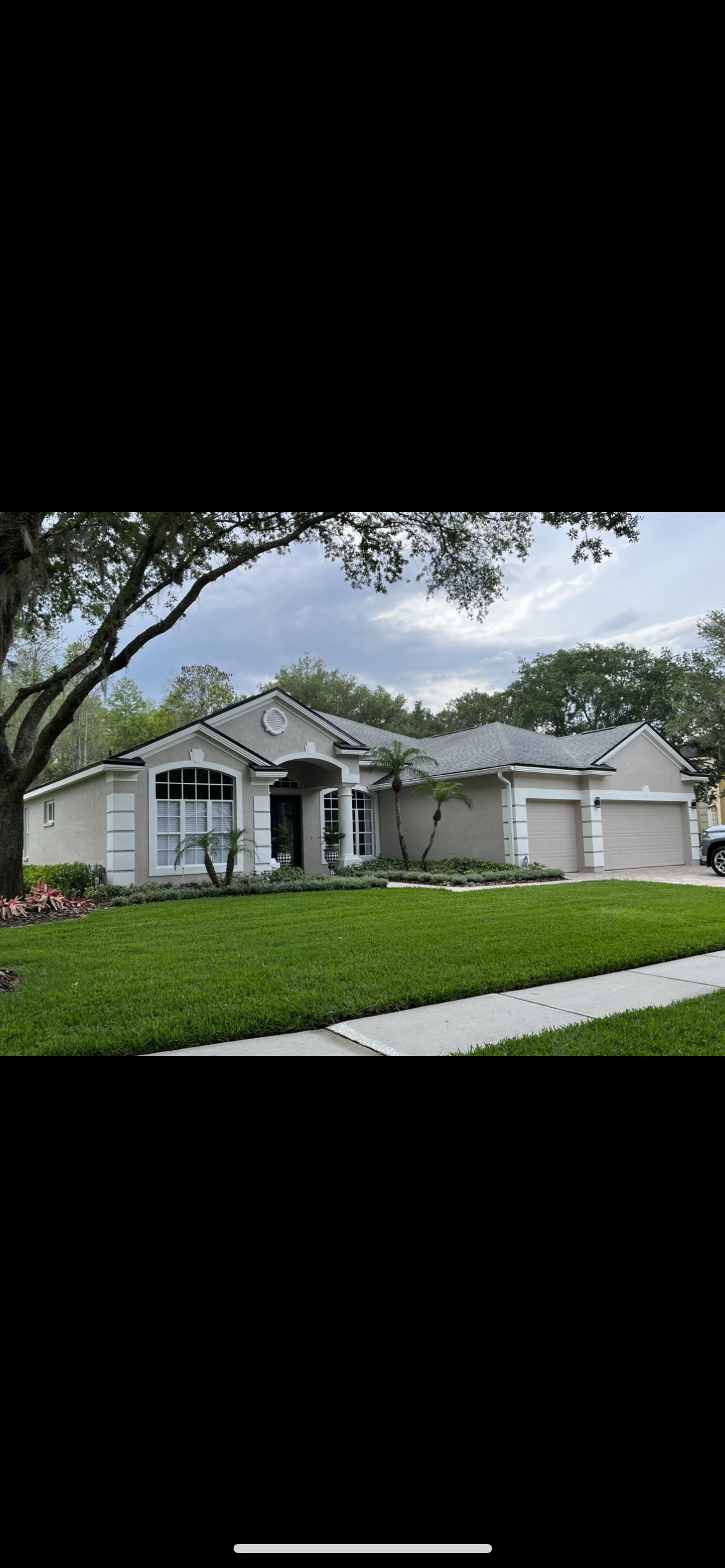 A single-story house with green grass and trees in front on a cloudy day.