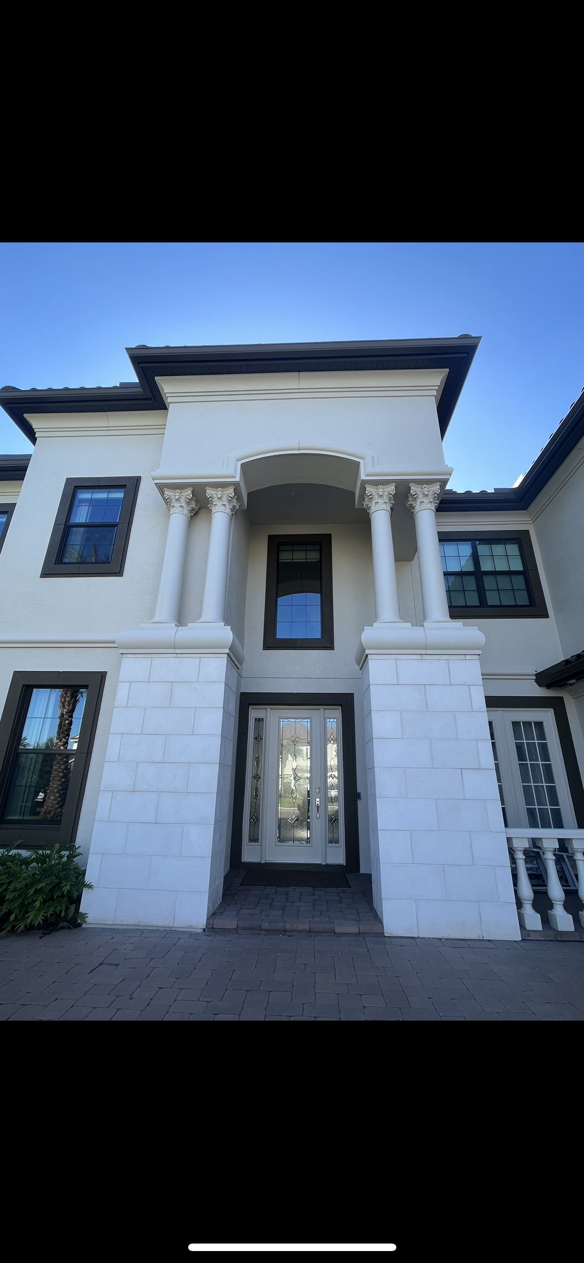 A white two-story house with columns flanking the front door under a blue sky.