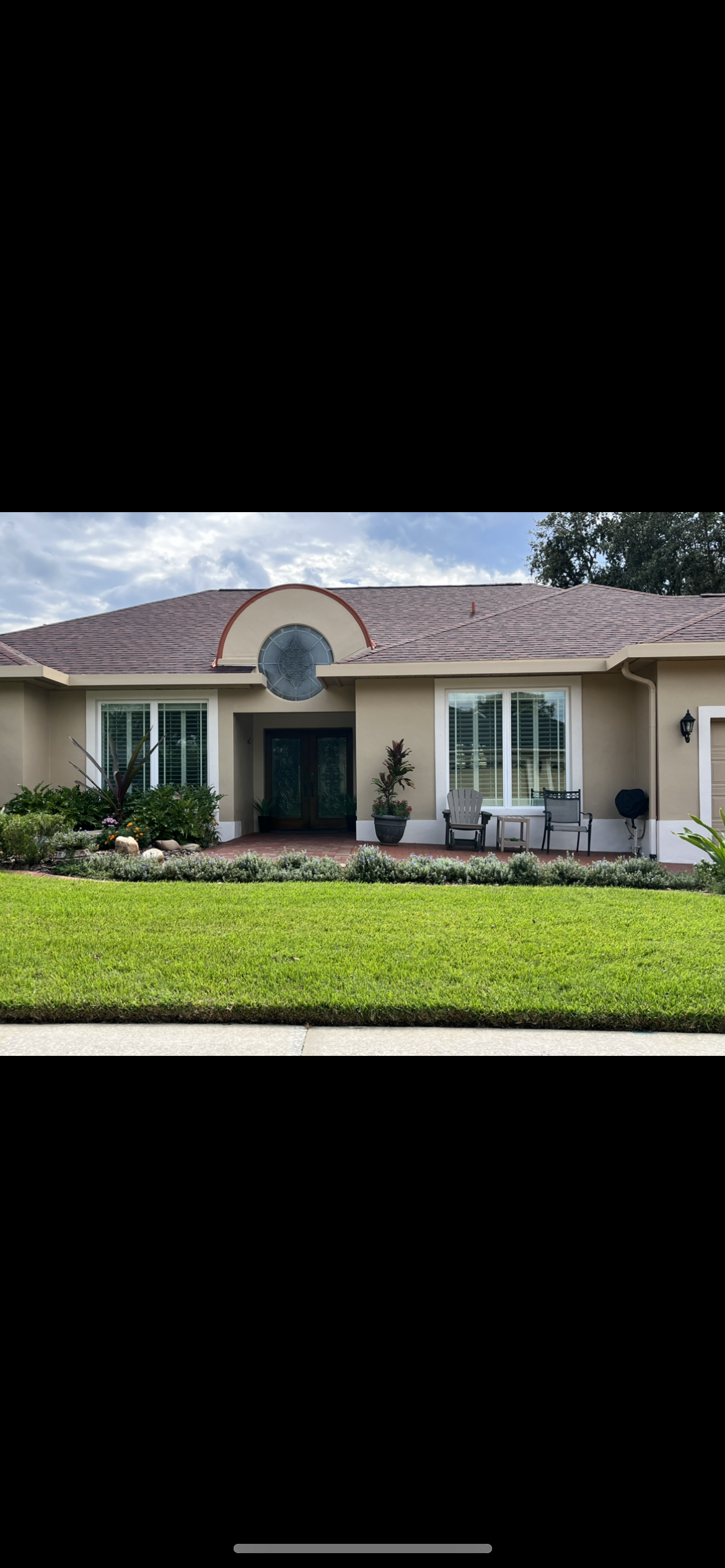 Beige single-story house with brown roof, green lawn, and arched window over the front door.