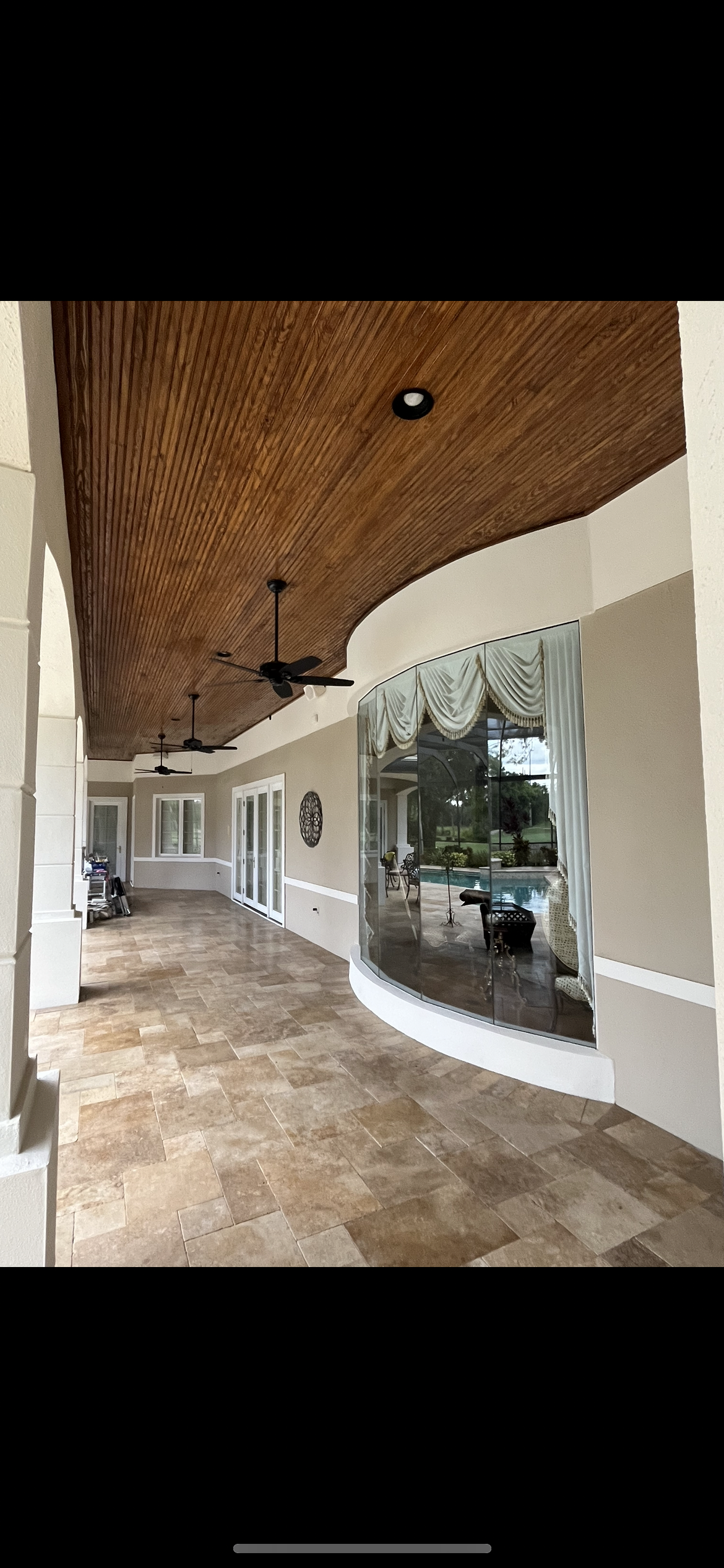 Exterior covered patio with textured wood ceiling, tile floor, glass wall, and ceiling fans.
