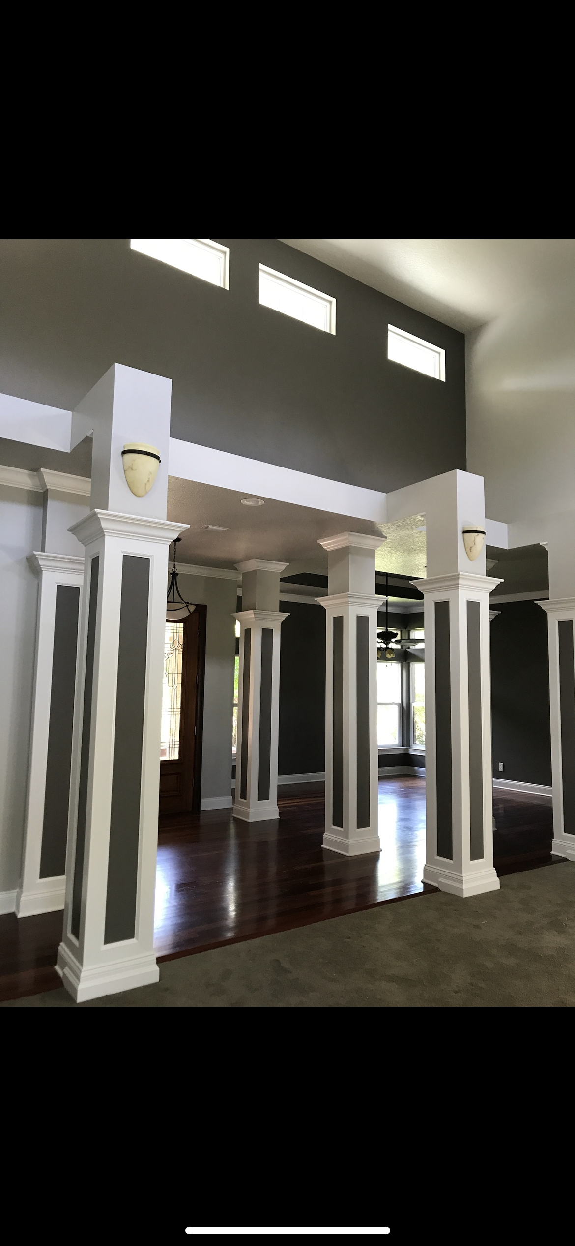 Interior view of a room with decorative white pillars with grey panels, dark wood floors, and neutral walls.