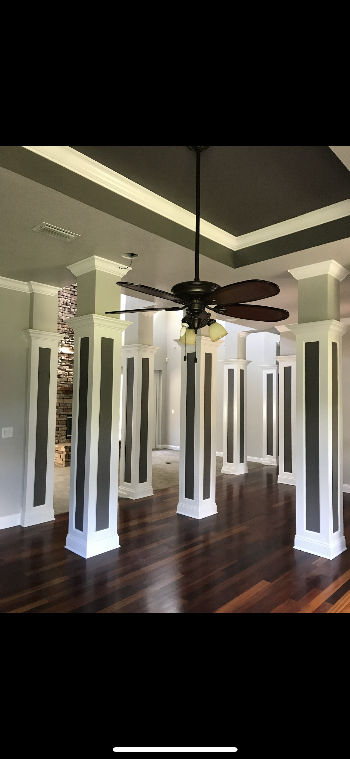 Large room with columns, dark wood floor, ceiling fan. The columns are white with dark gray vertical stripes.