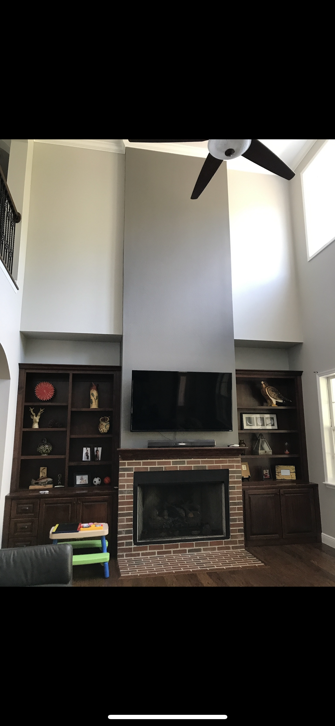Living room with fireplace, built-in shelves, TV, and high ceilings. Brown, grey, and white colors.
