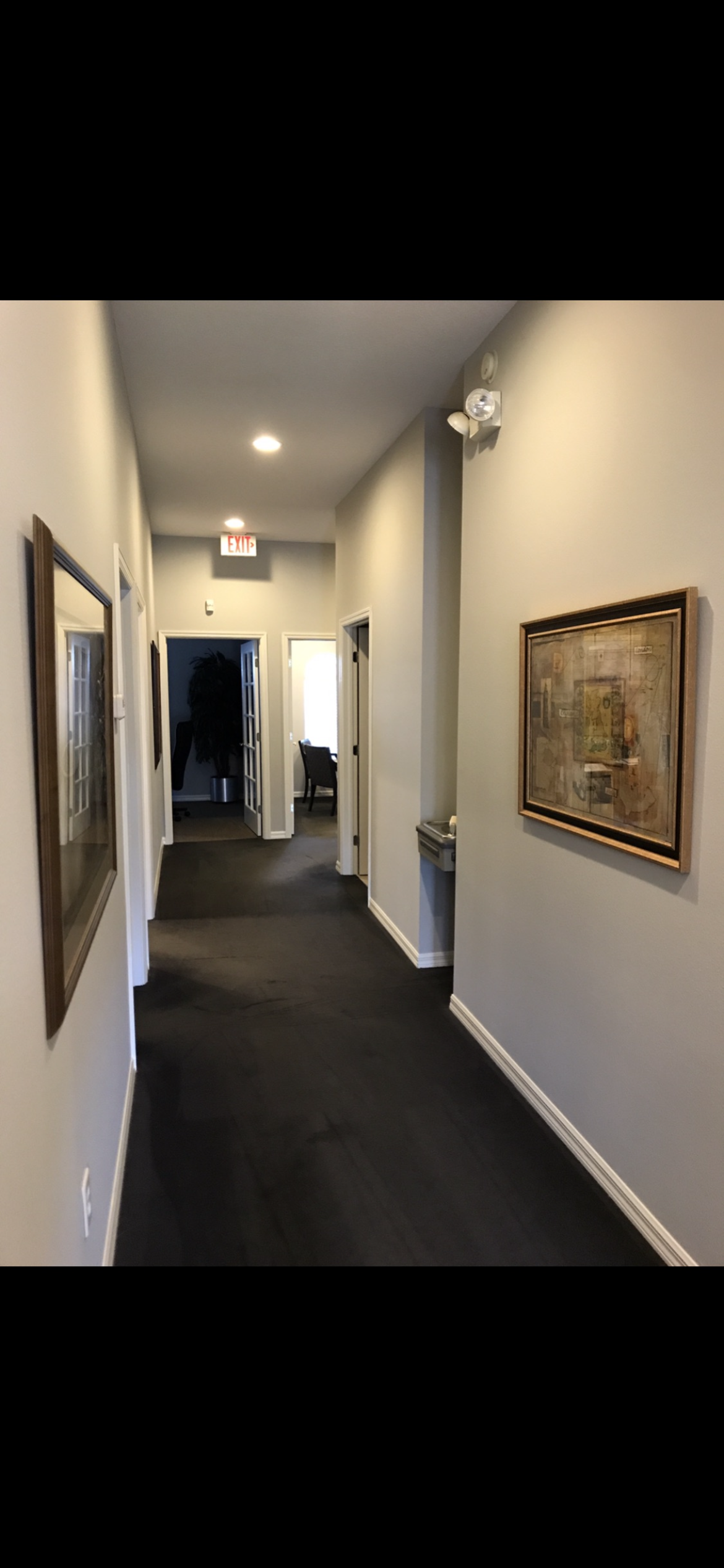 Long, narrow hallway with dark carpet, framed mirror on the left, and art on the right.