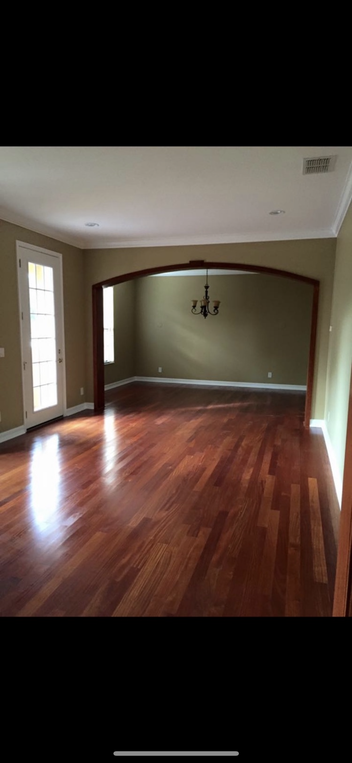 Interior of a house with hardwood floors, olive green walls, and a chandelier. A wooden archway leads to another room.