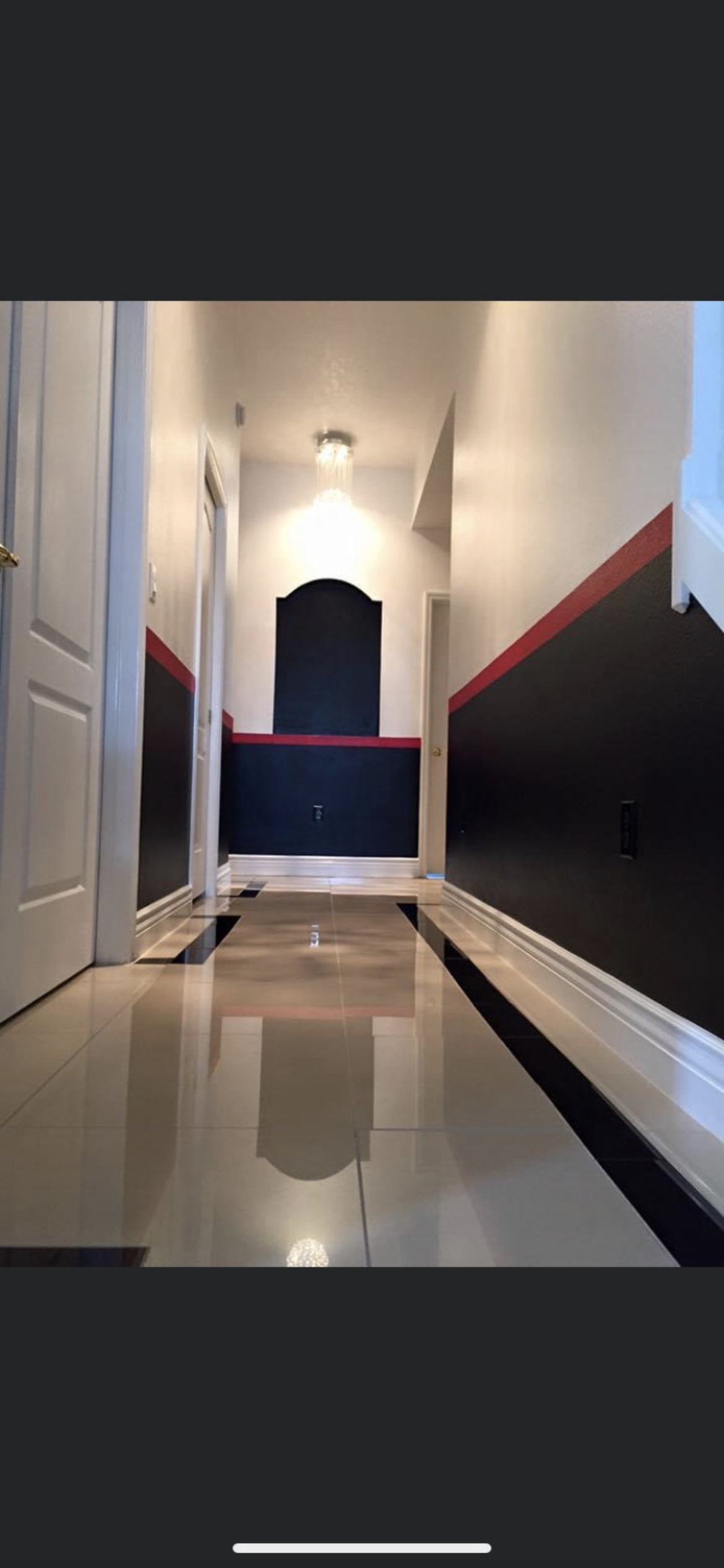 Long hallway with shiny floor, black and white walls with red accents, and a rounded doorway at the end.