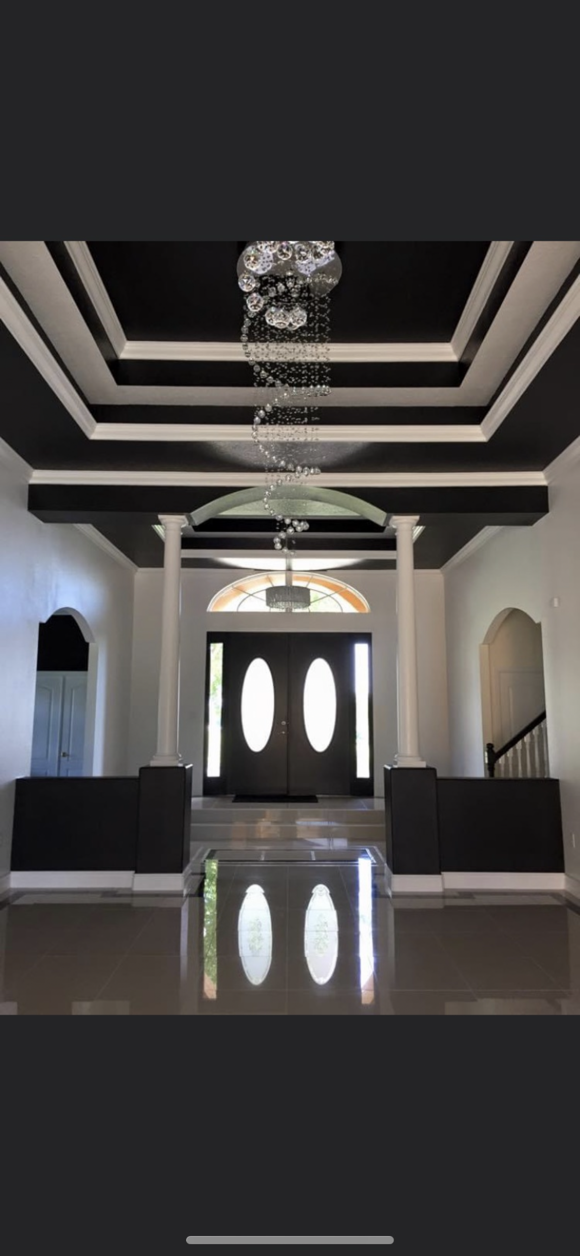 Grand foyer with a chandelier, dark door, columns, and a reflective floor.