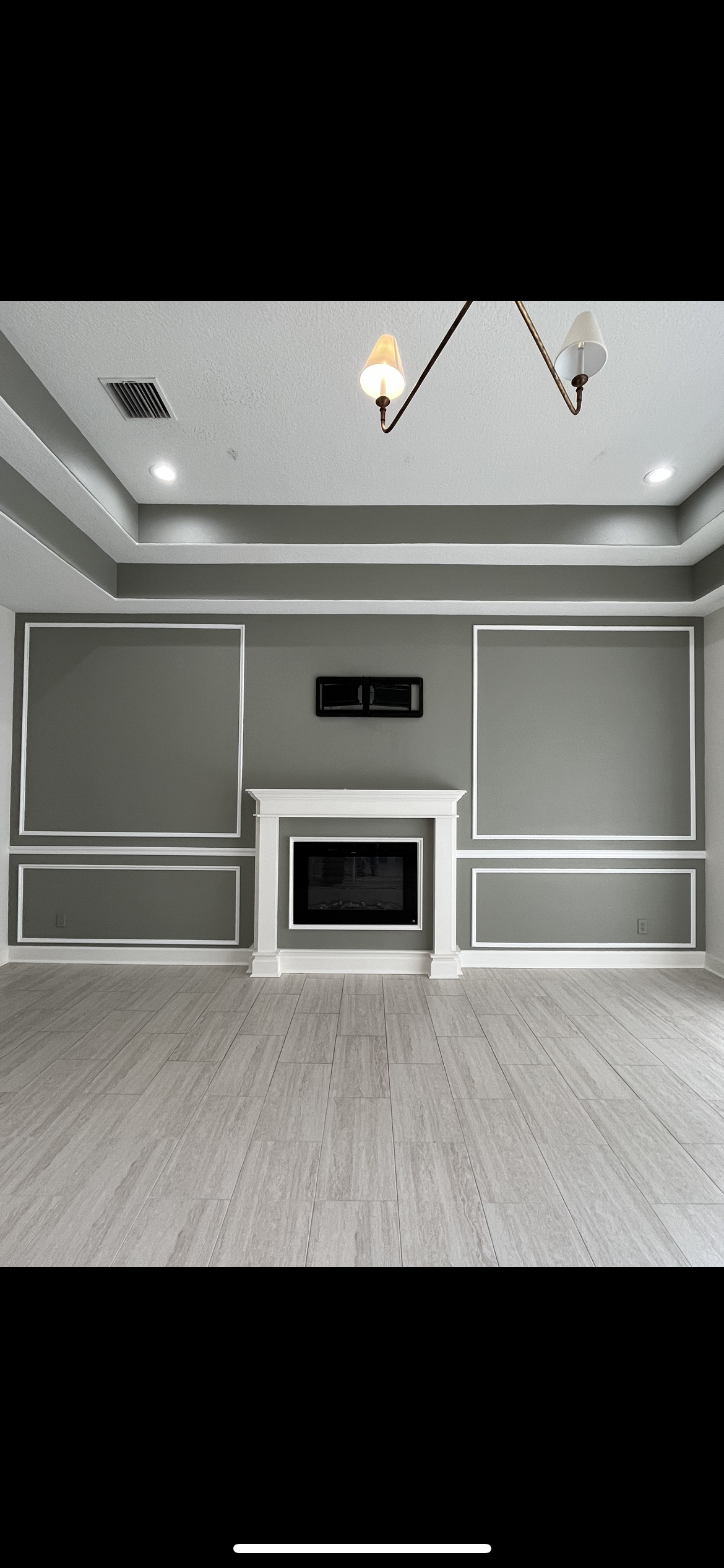 Gray living room with fireplace, accent wall, and wood-look flooring. Chandelier hangs from ceiling.
