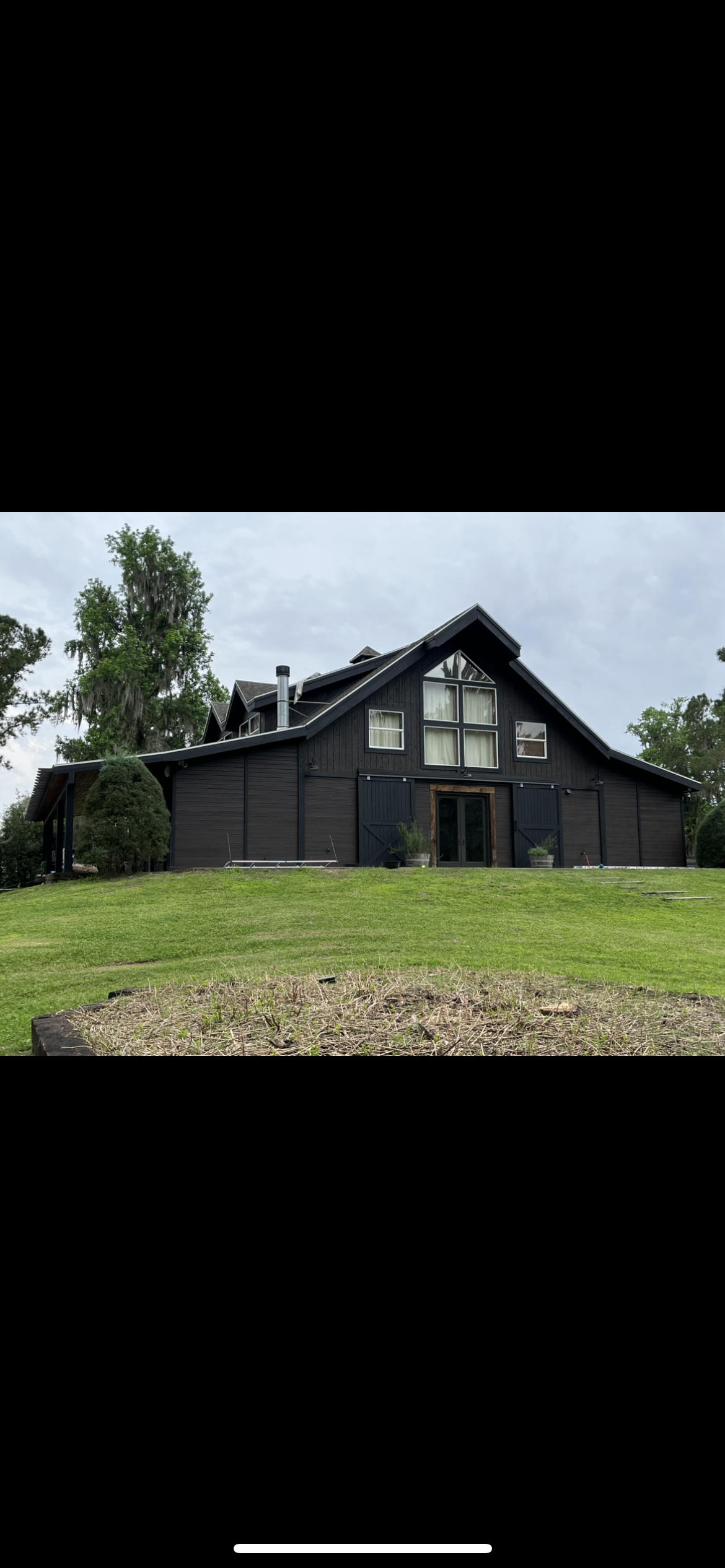 Dark brown barn-style building on a grassy hill under an overcast sky.
