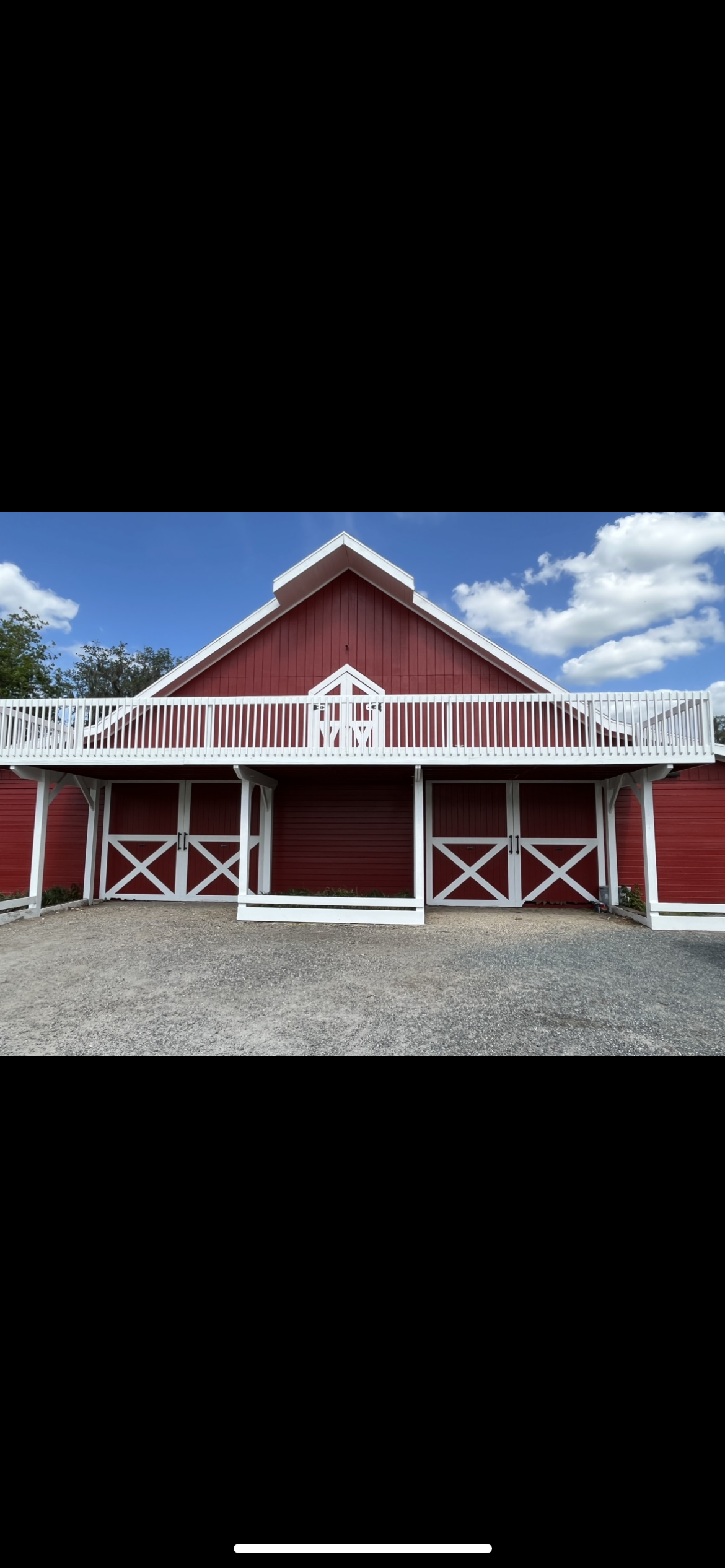 Red barn with white trim, doors, and a balcony against a blue sky with clouds.