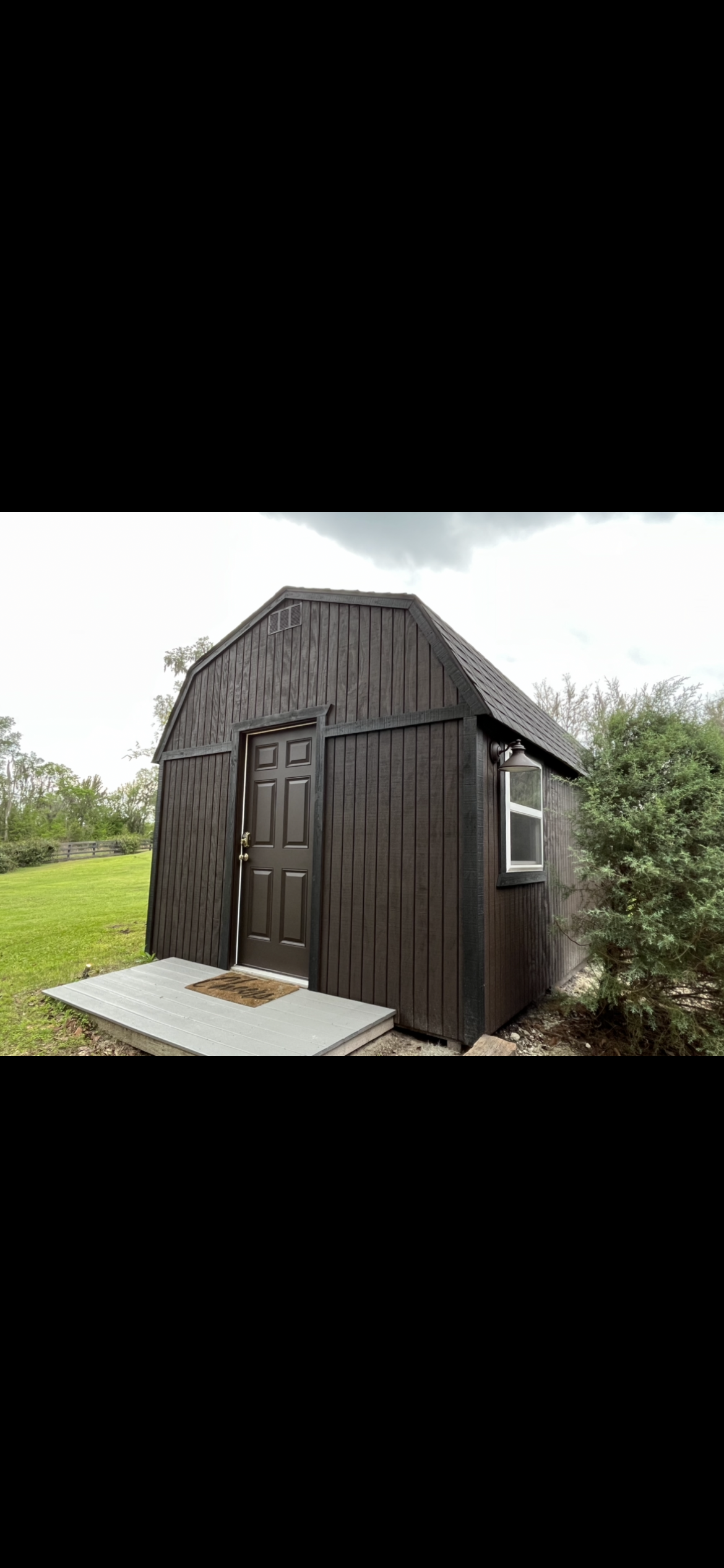 Dark brown shed with a concrete step in a grassy area.