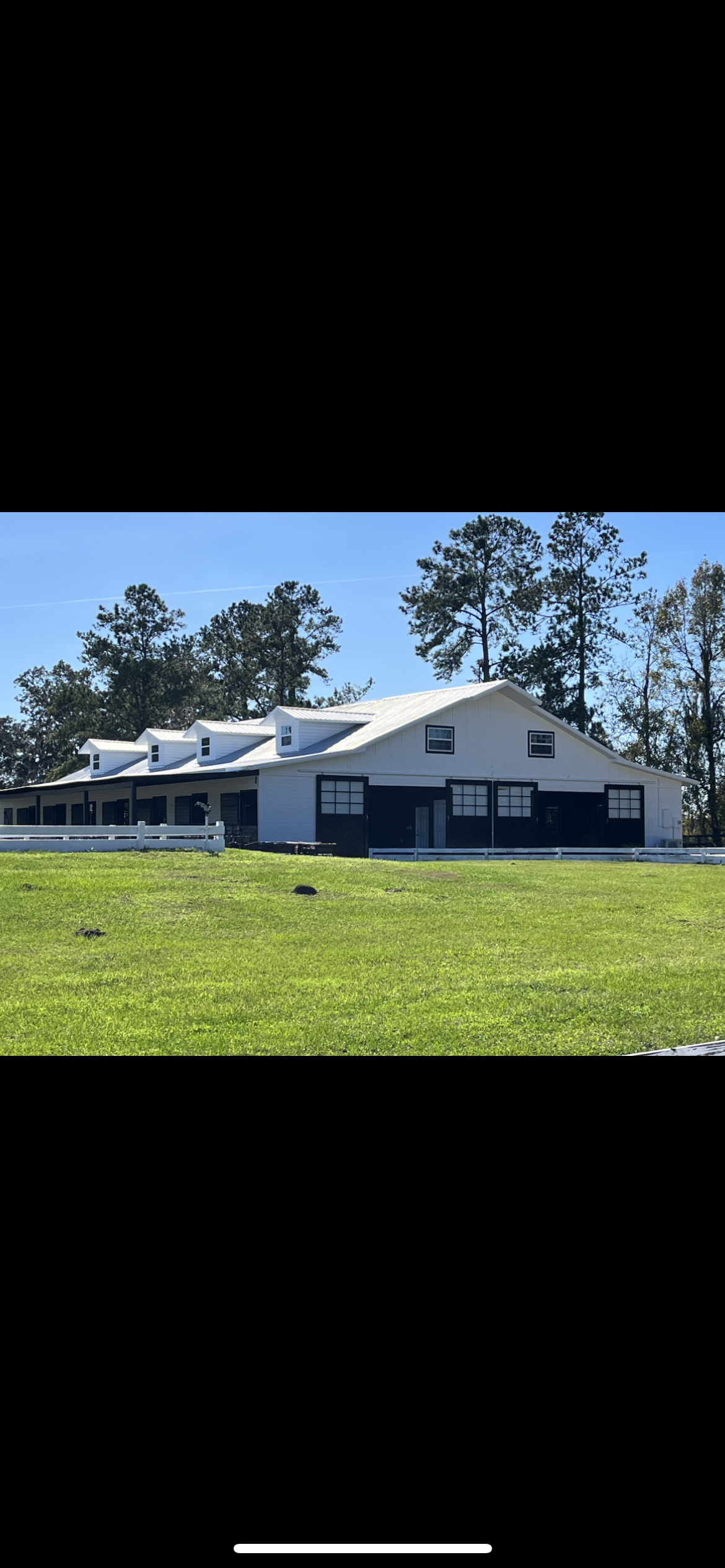A white barn-style building with a green lawn and trees under a blue sky.