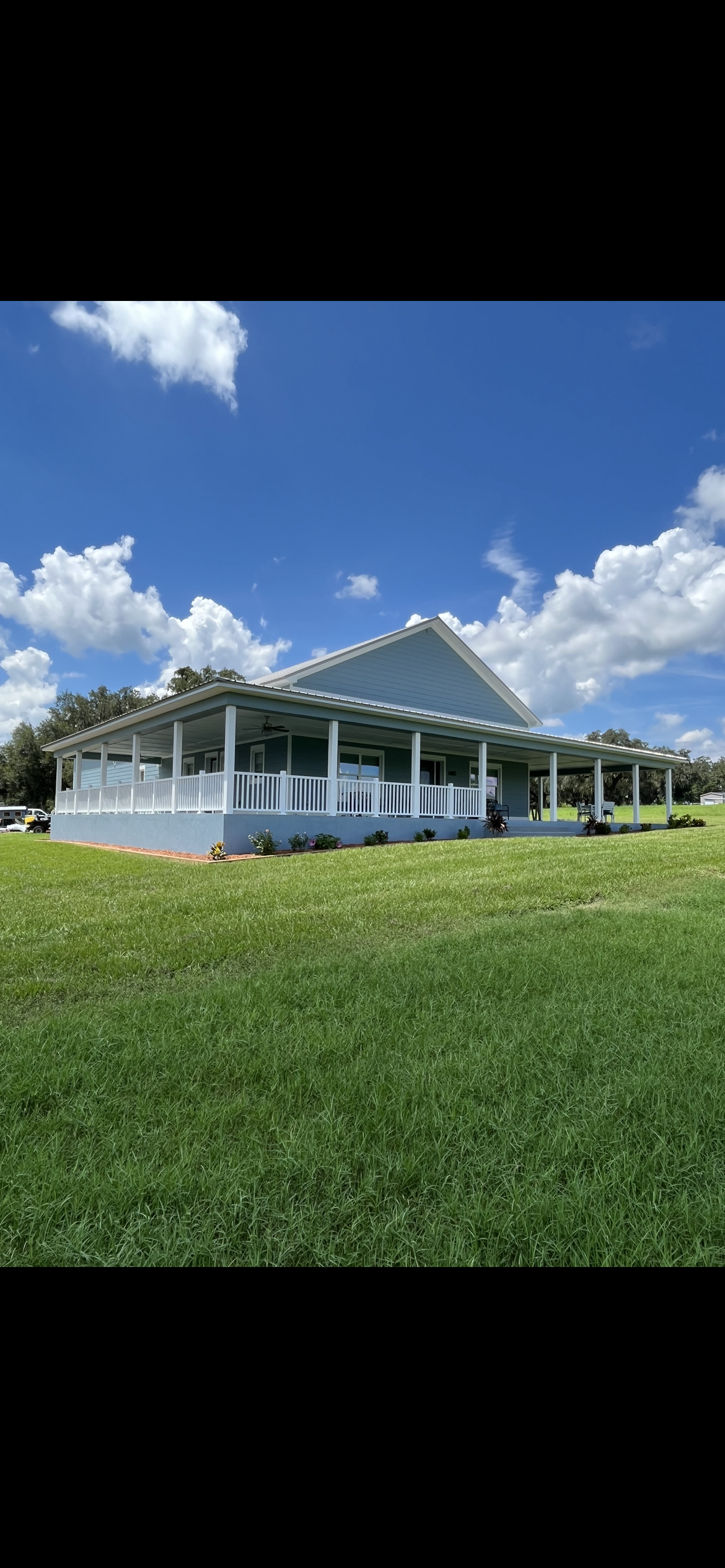 Light blue building with white pillars and roof on a grassy field under a blue sky with clouds.