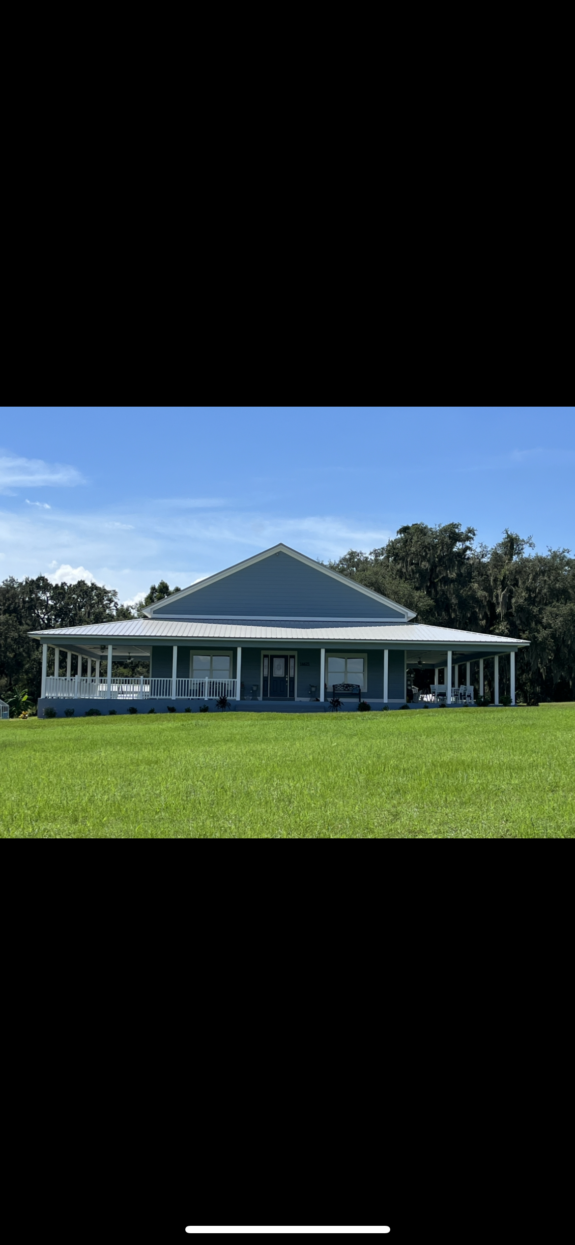 Light blue house with a long porch on a grassy field under a blue sky.