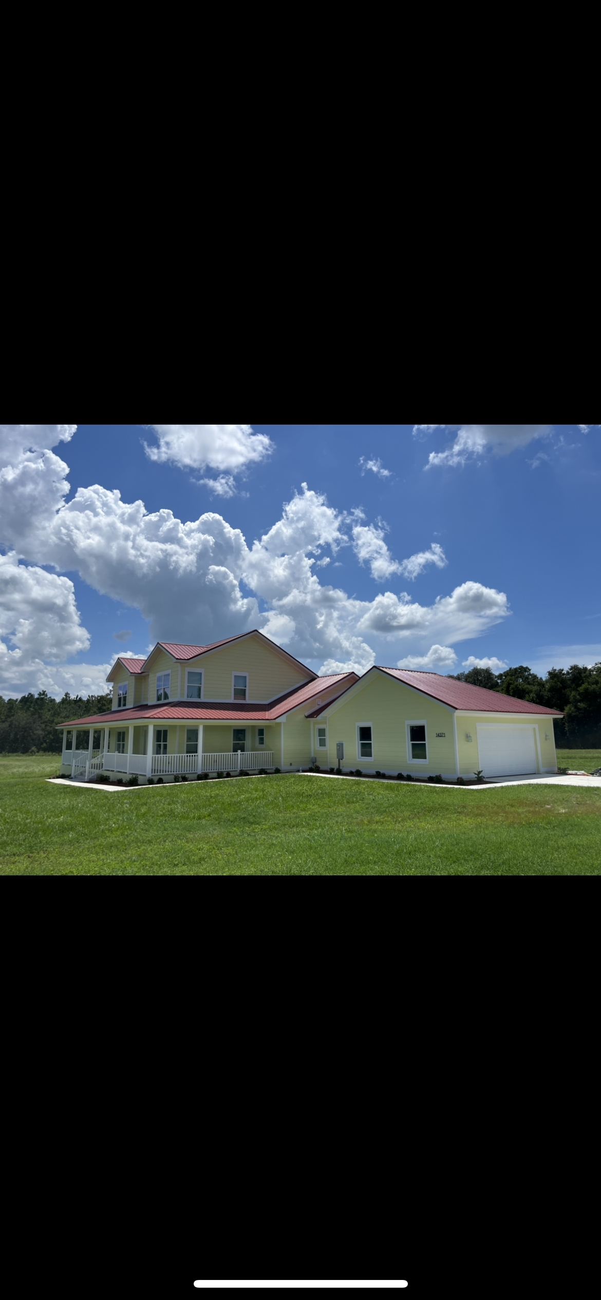 A large yellow house with a red roof, a wrap-around porch, and a green lawn under a blue sky.
