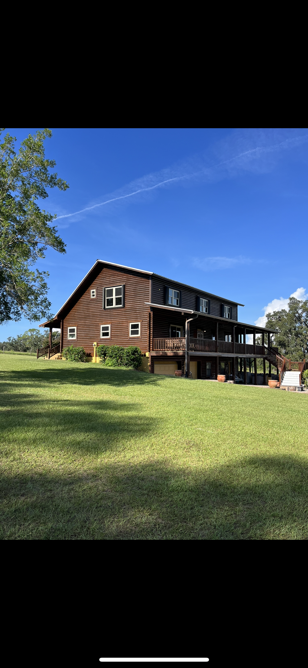 Brown wooden barn-style house with multiple stories, large porch, and green lawn under a clear blue sky.