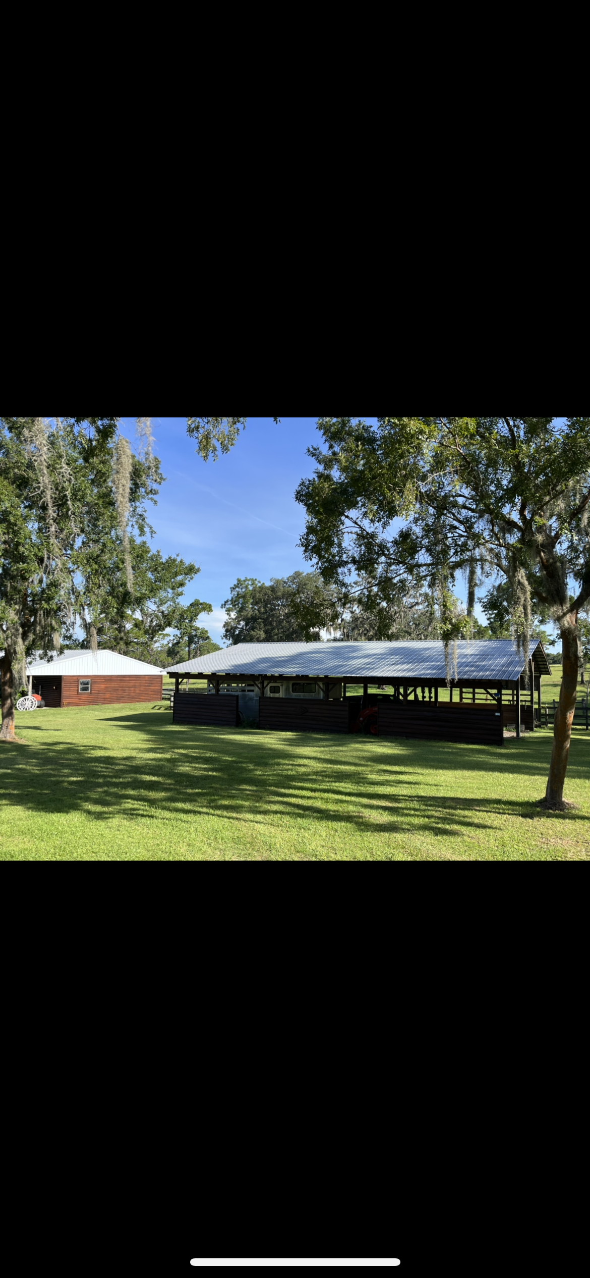 A grassy field with a large open-air pavilion and a brick building under a clear sky.