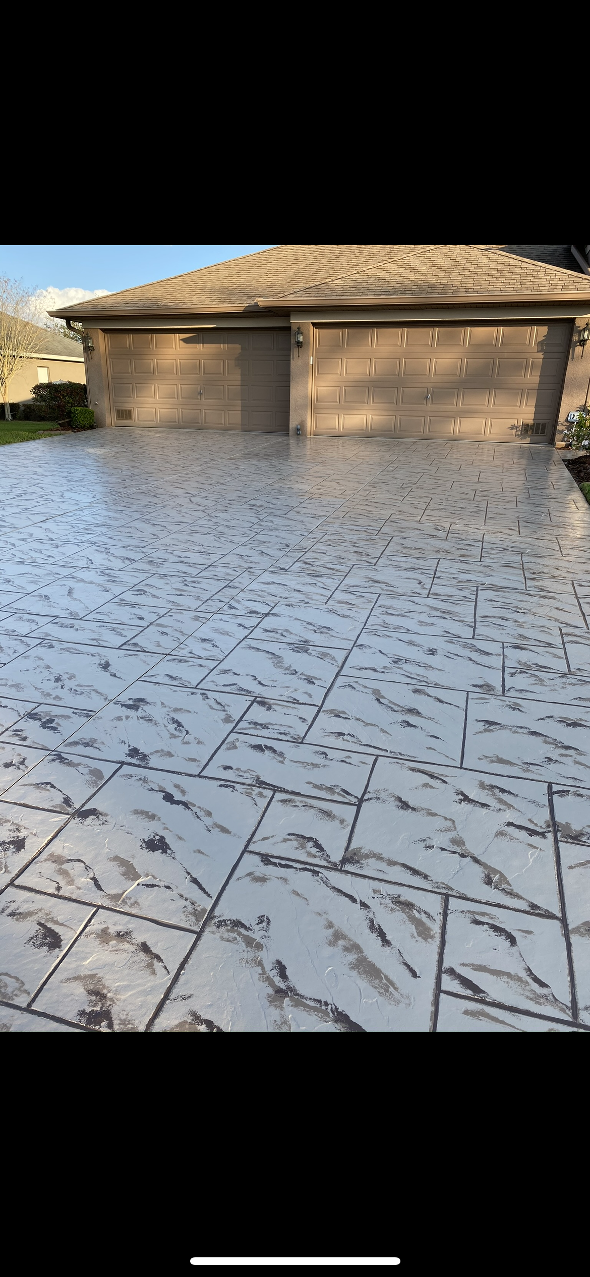 A driveway paved with a marbled pattern leads up to a brown garage with two doors.