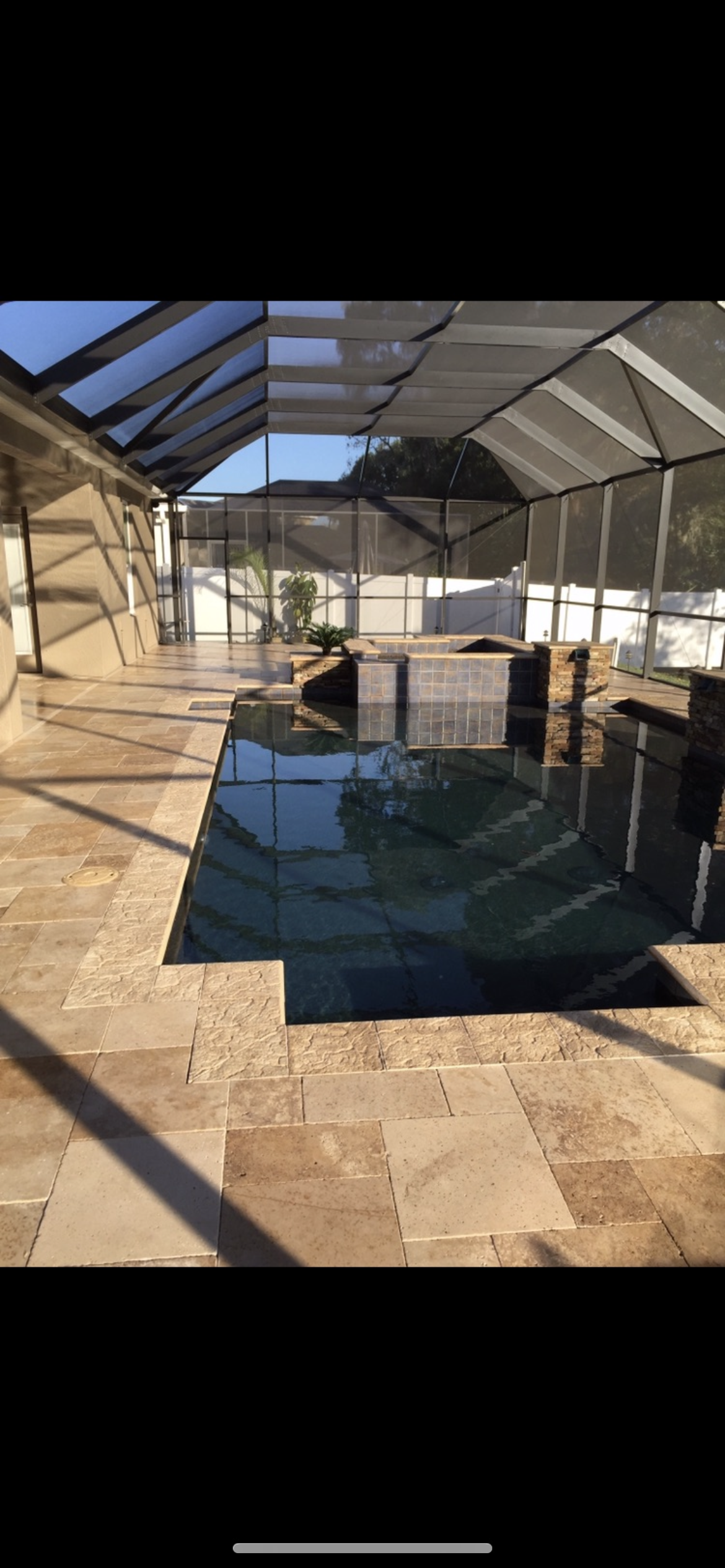 Pool area with screened enclosure, stone pavers, and water.