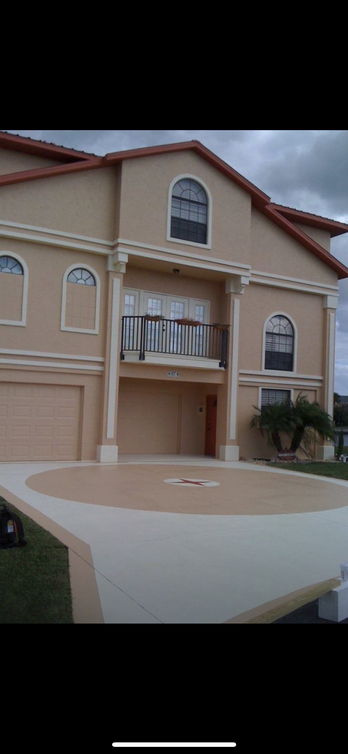 Tan stucco house with arched windows, a balcony, and a circular driveway.