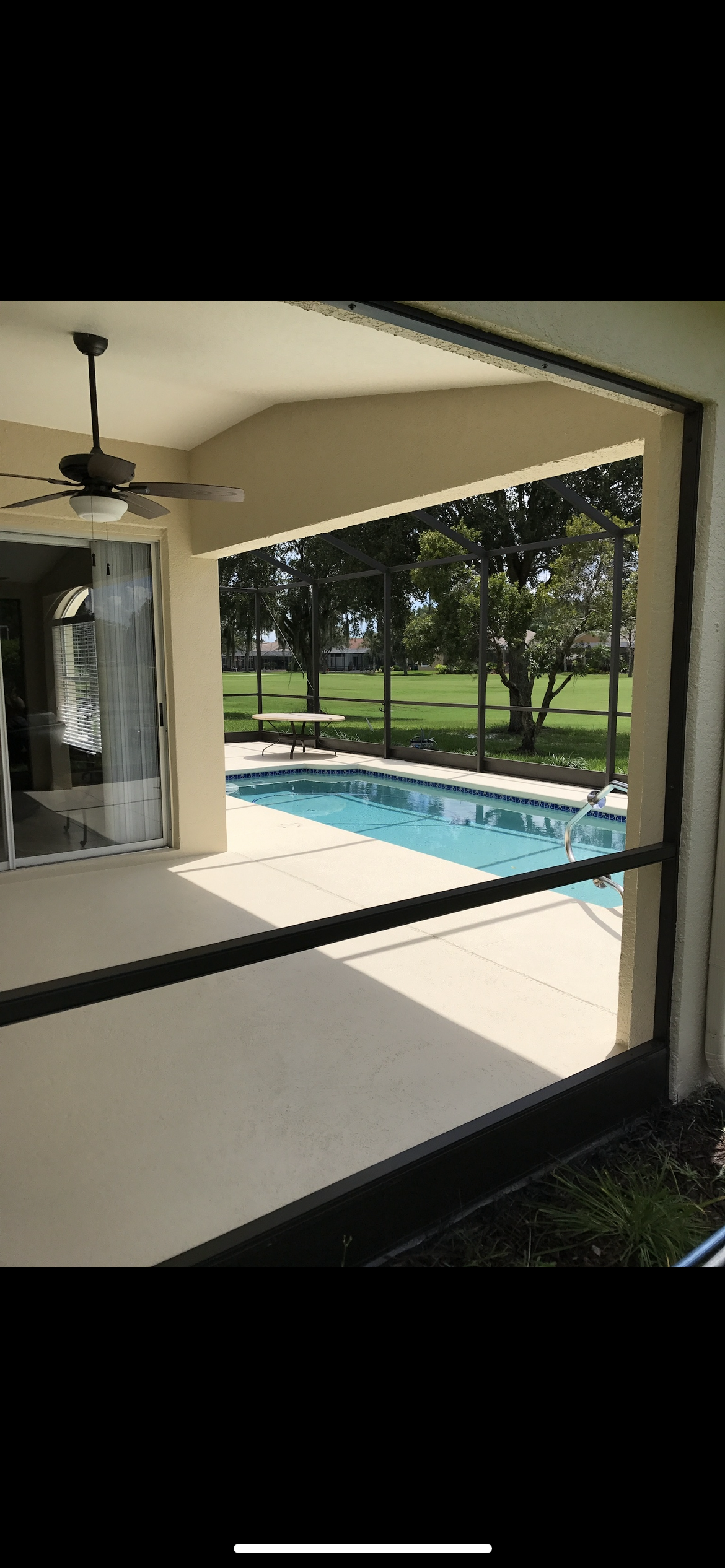 A covered patio overlooking a pool, with trees and a green lawn in the background.