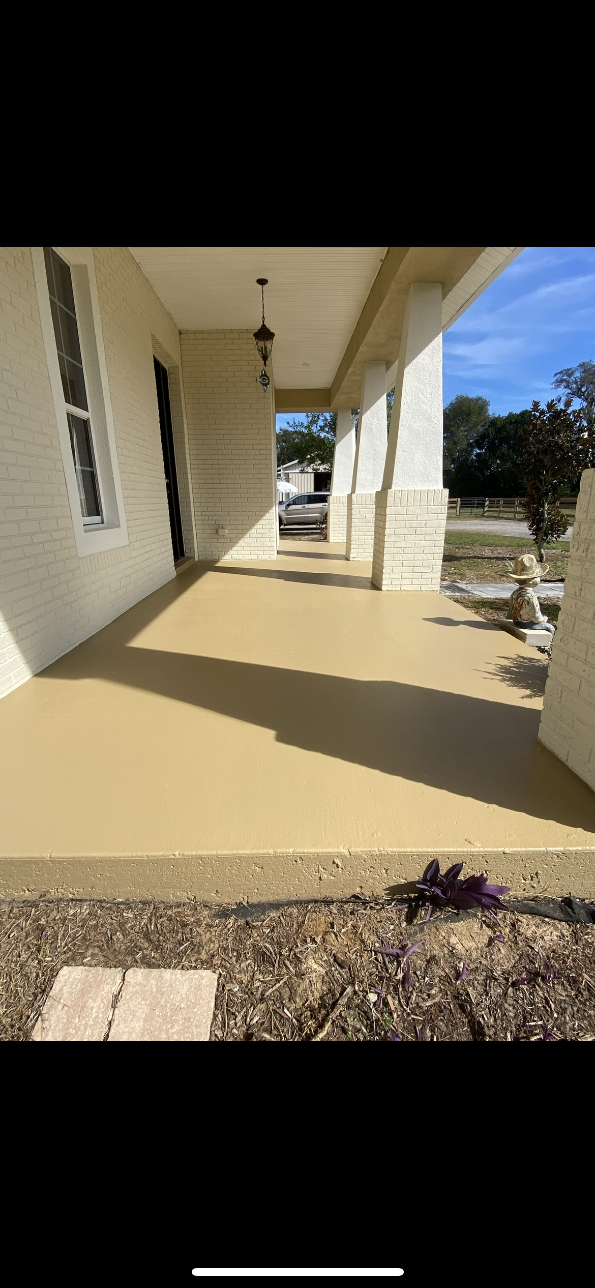 A covered porch with white columns, a tan floor, and a view of a street.