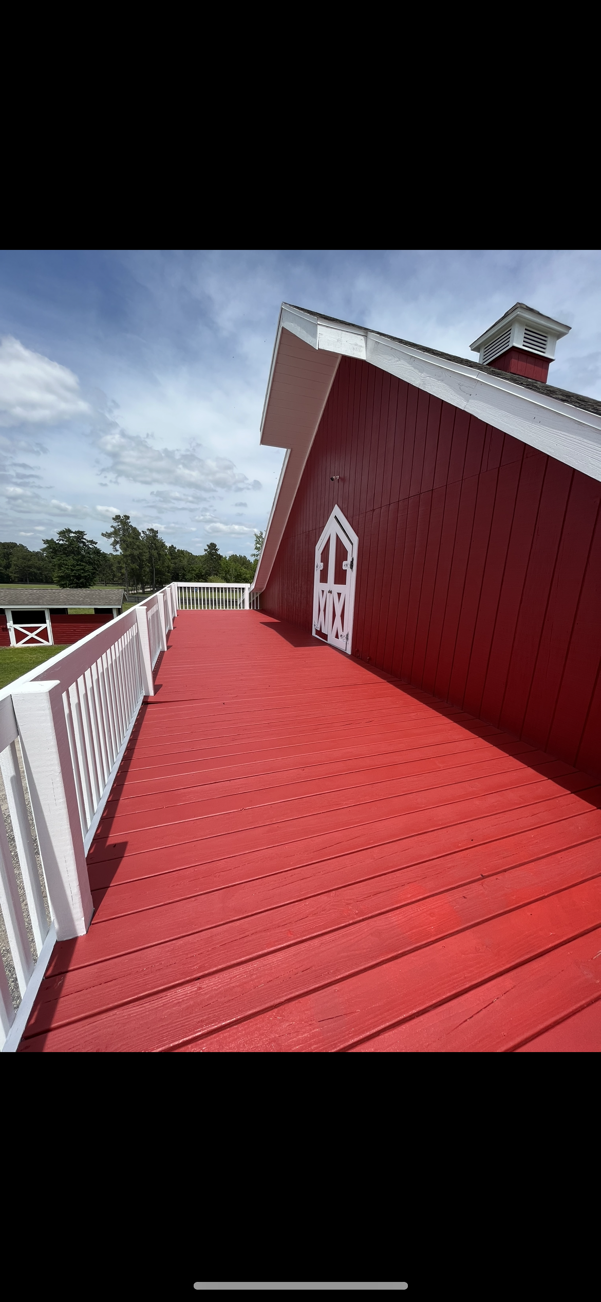 Red barn with a white railing and a red deck on a sunny day.
