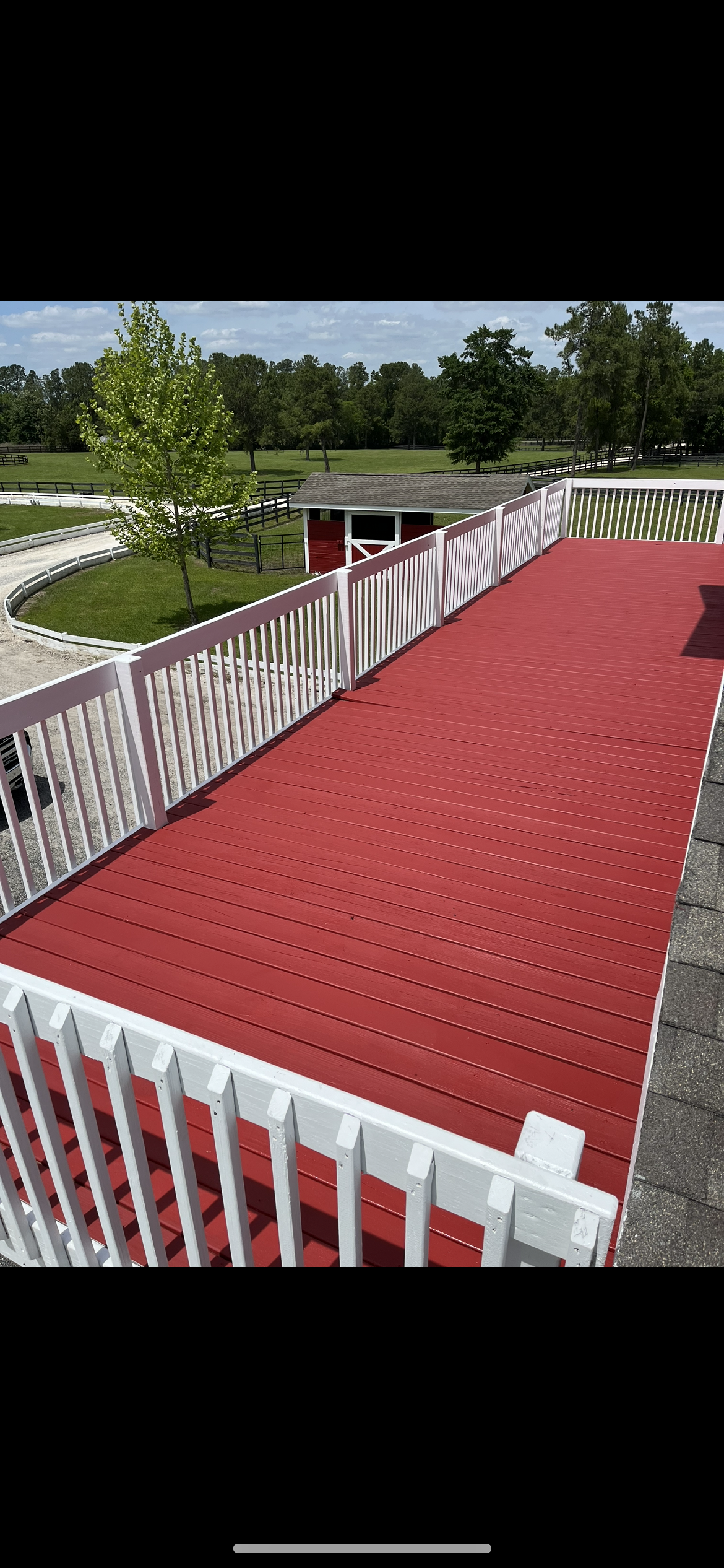 Red deck with white railing overlooks a green lawn and trees under a sunny sky.