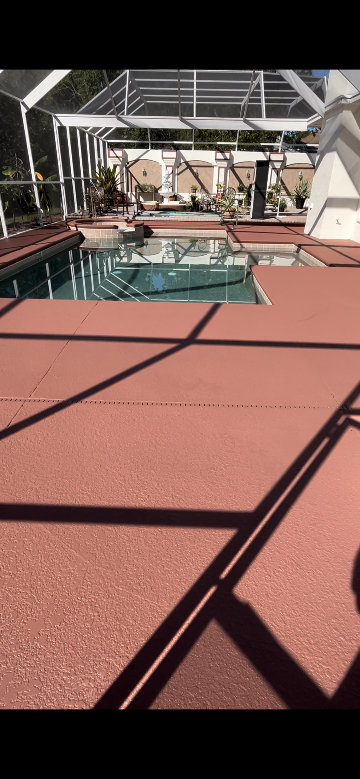 Swimming pool with a screen enclosure, red deck, and a sunny day.