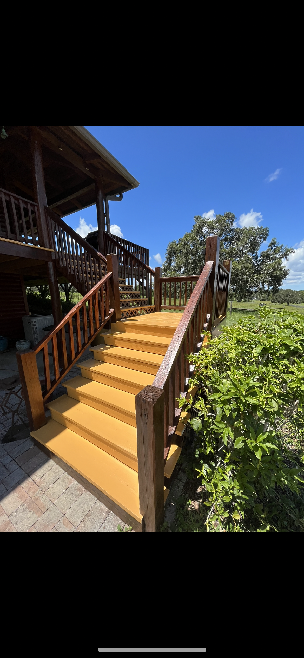Wooden stairs painted yellow leading up to a wooden deck with a blue sky background.
