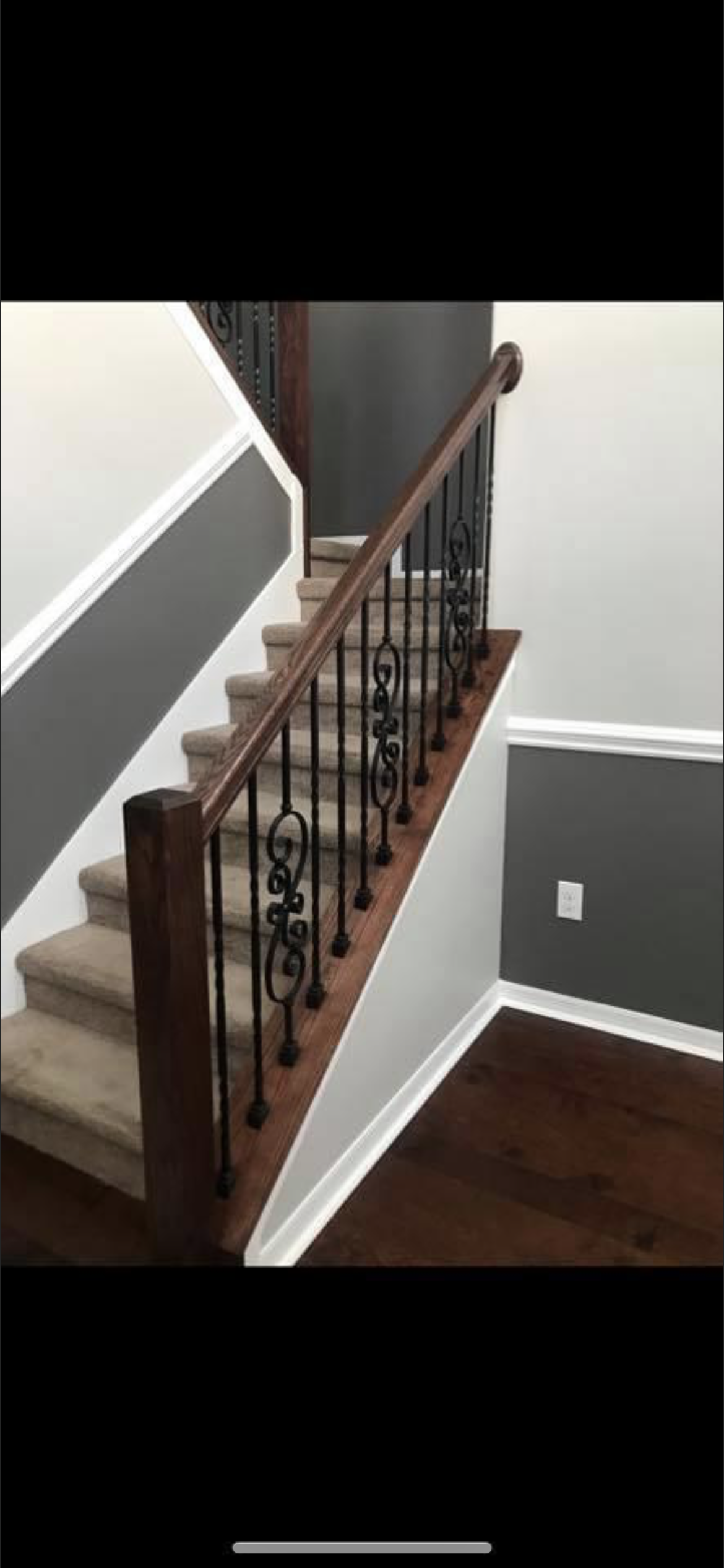 A staircase with wooden steps, a dark handrail, and black iron balusters. The walls are gray and white.