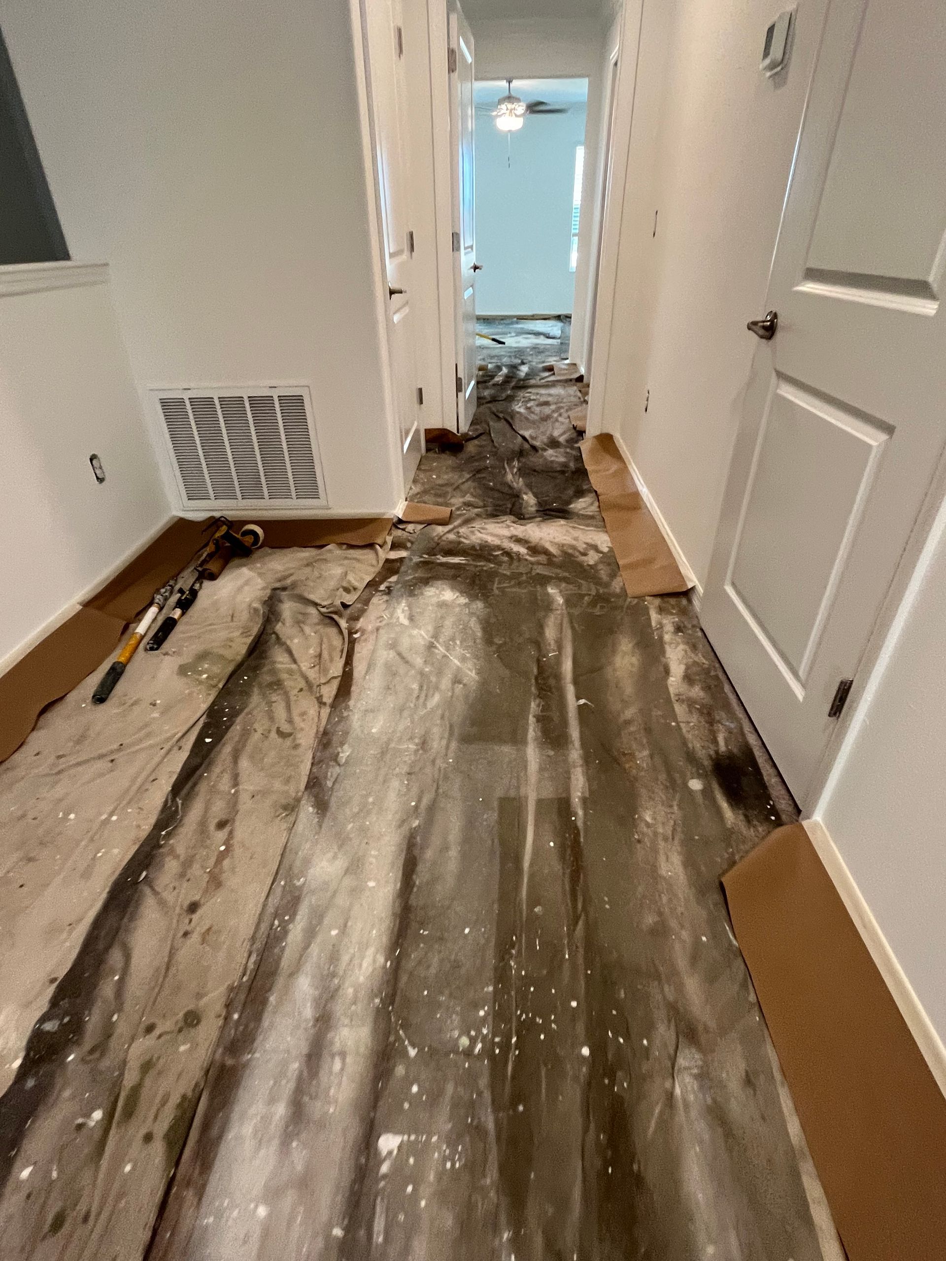 Hallway with floor demolition in progress. Exposed concrete and debris with cardboard protection along walls.